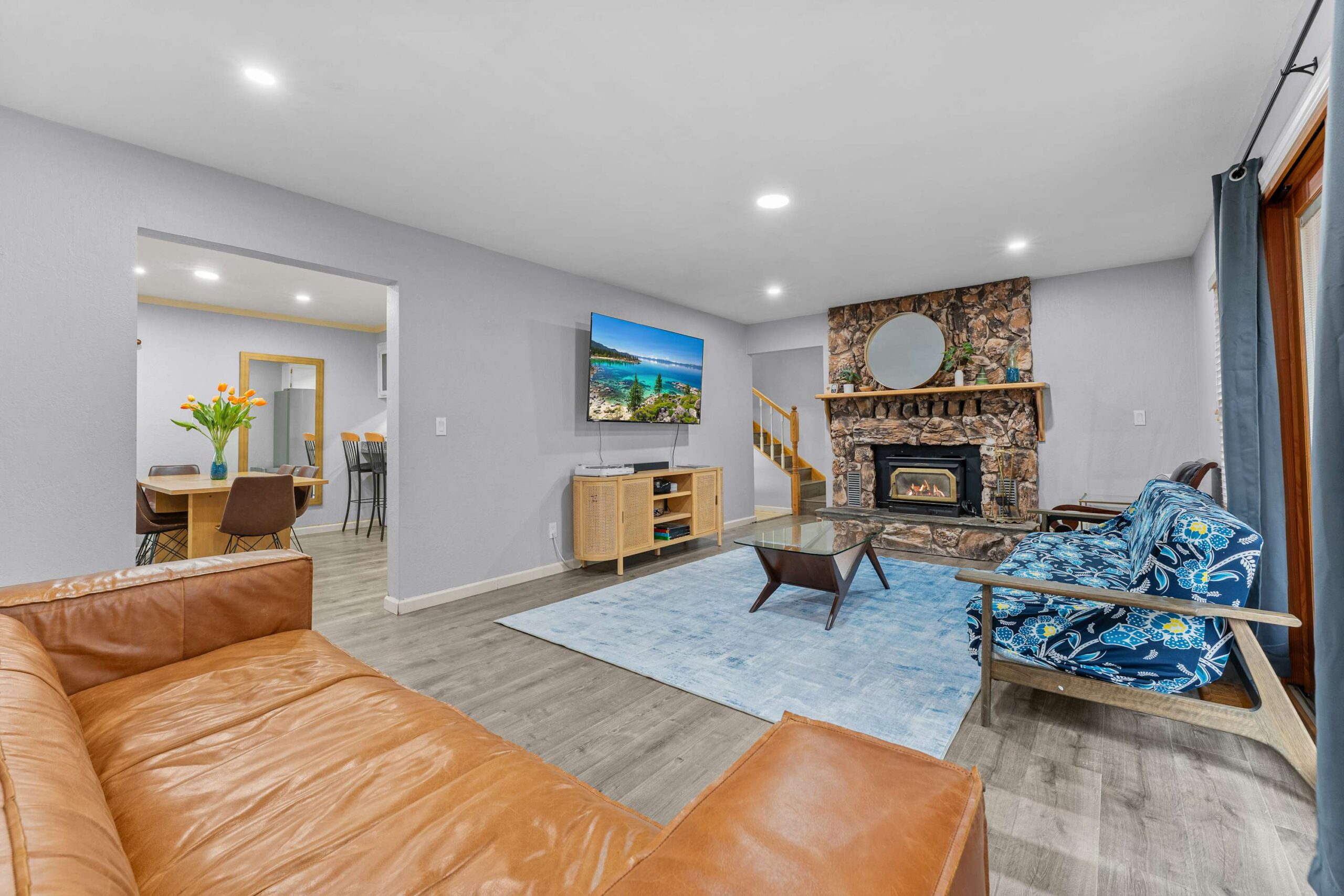 Cozy Truckee vacation rental living room with a stone fireplace, leather sofa, blue rug, TV, and dining area view.