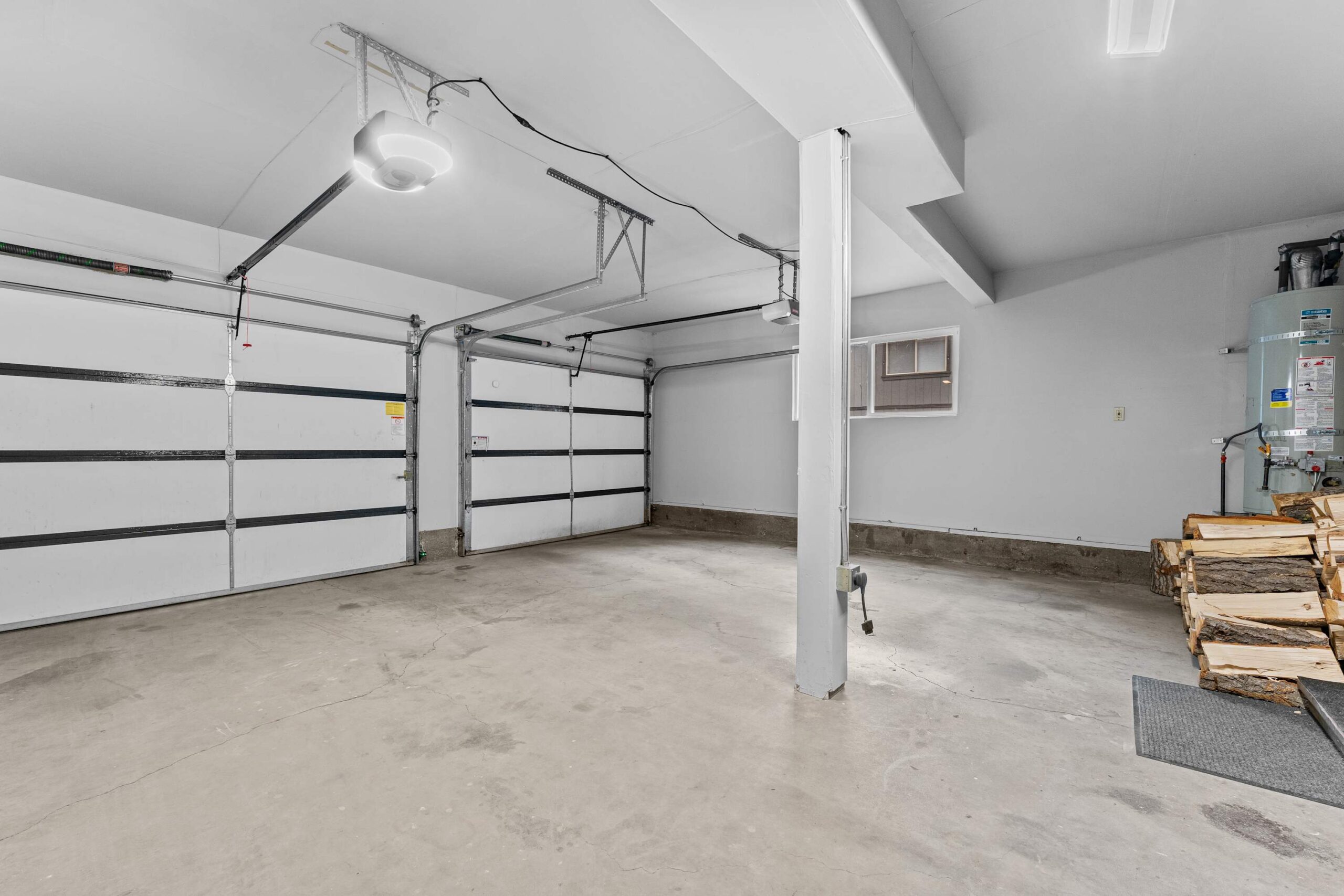 Spacious garage in Truckee vacation rental, featuring dual white doors, furnace, and stacked firewood in a modern setting.