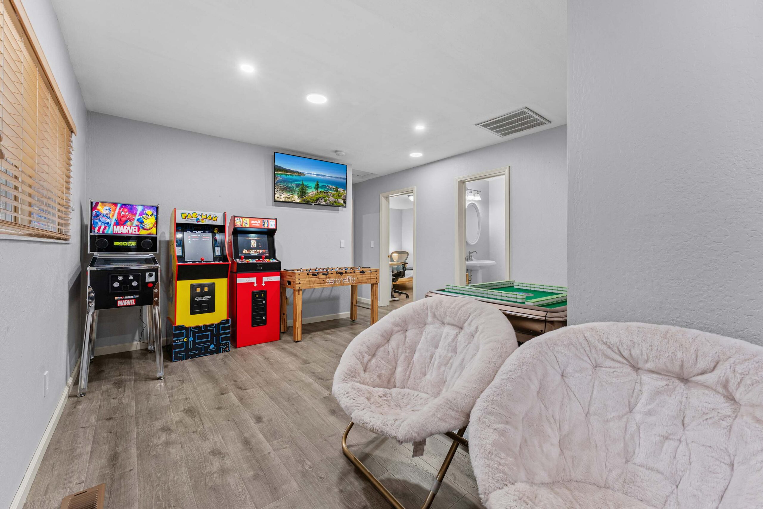 Cozy game room in a Truckee vacation rental, featuring arcade machines, foosball, plush chairs, and a scenic wall photo.