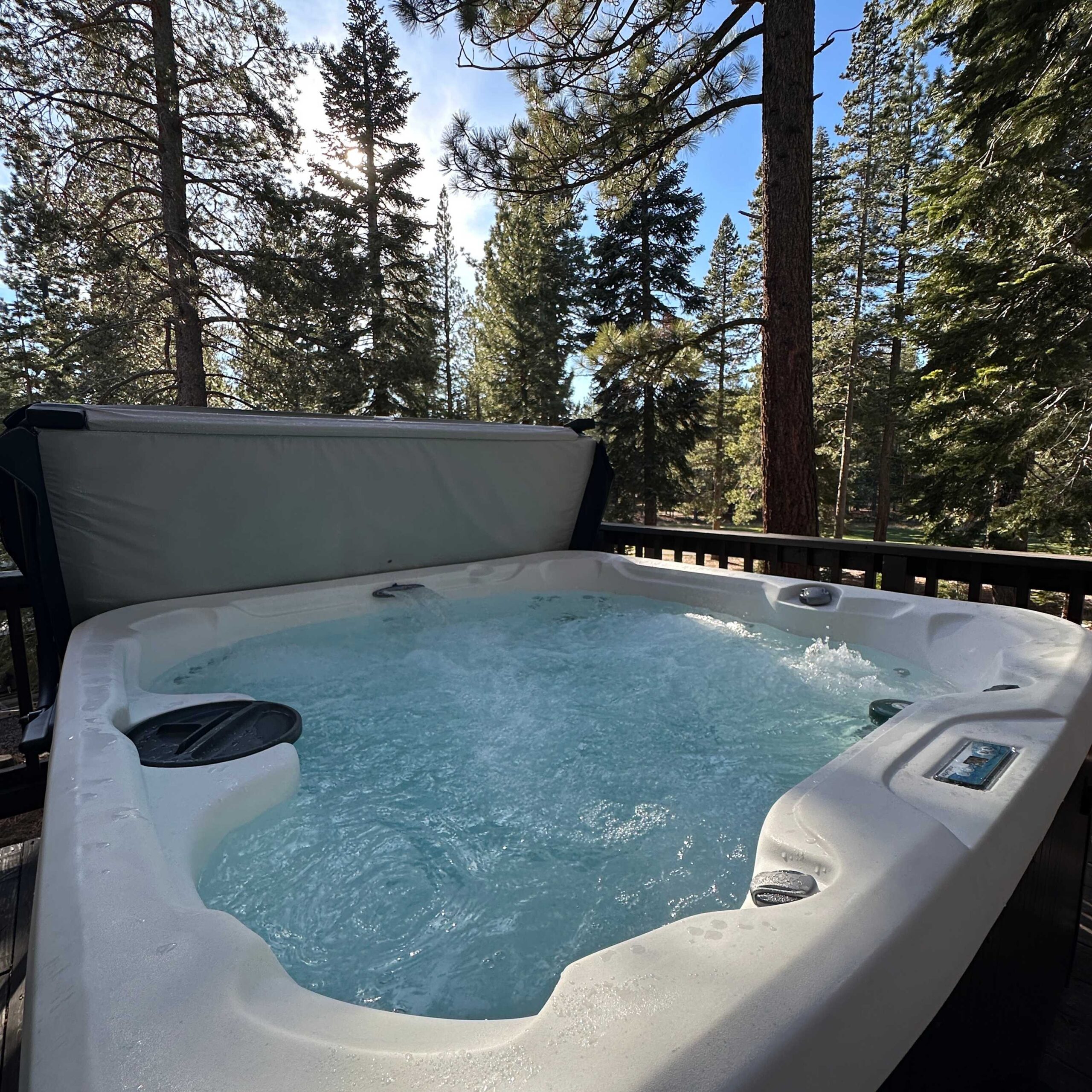 Hot tub on a deck surrounded by pine trees at a Truckee vacation rental, with clear skies and sunlight filtering through.