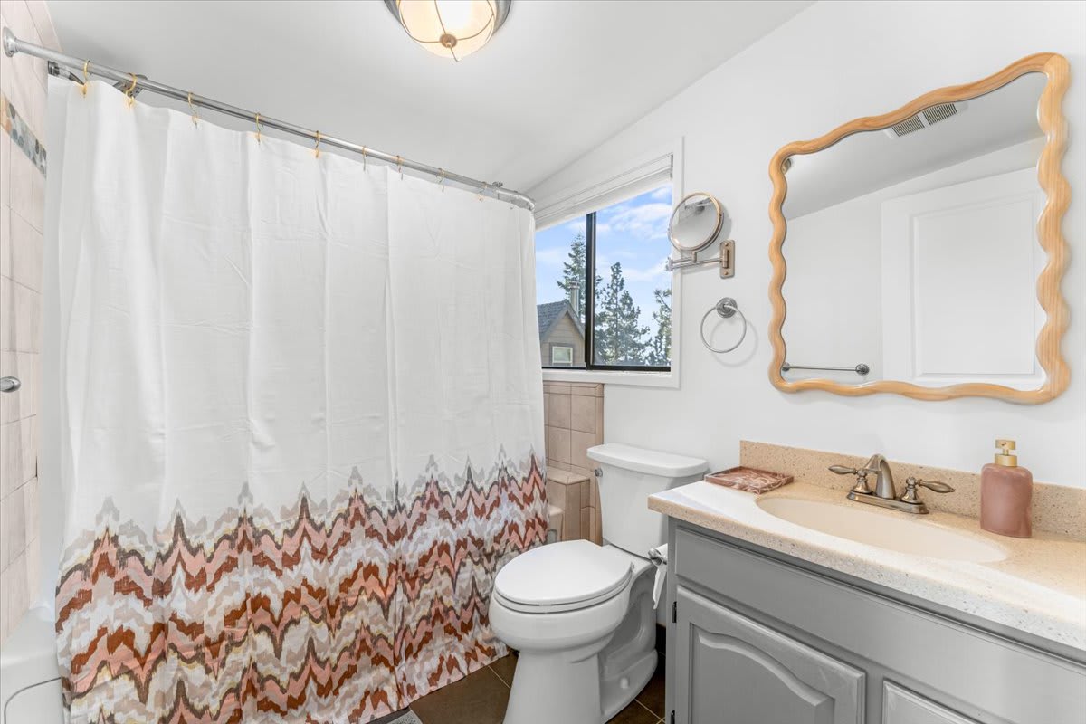 Kings Beach vacation rental bathroom with patterned shower curtain, a window view, and stylish mirror and sink.