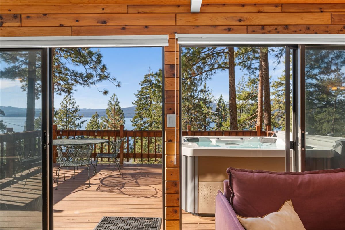 Kings Beach vacation rental with stunning lake view, cozy deck seating, and a hot tub amidst pine trees.