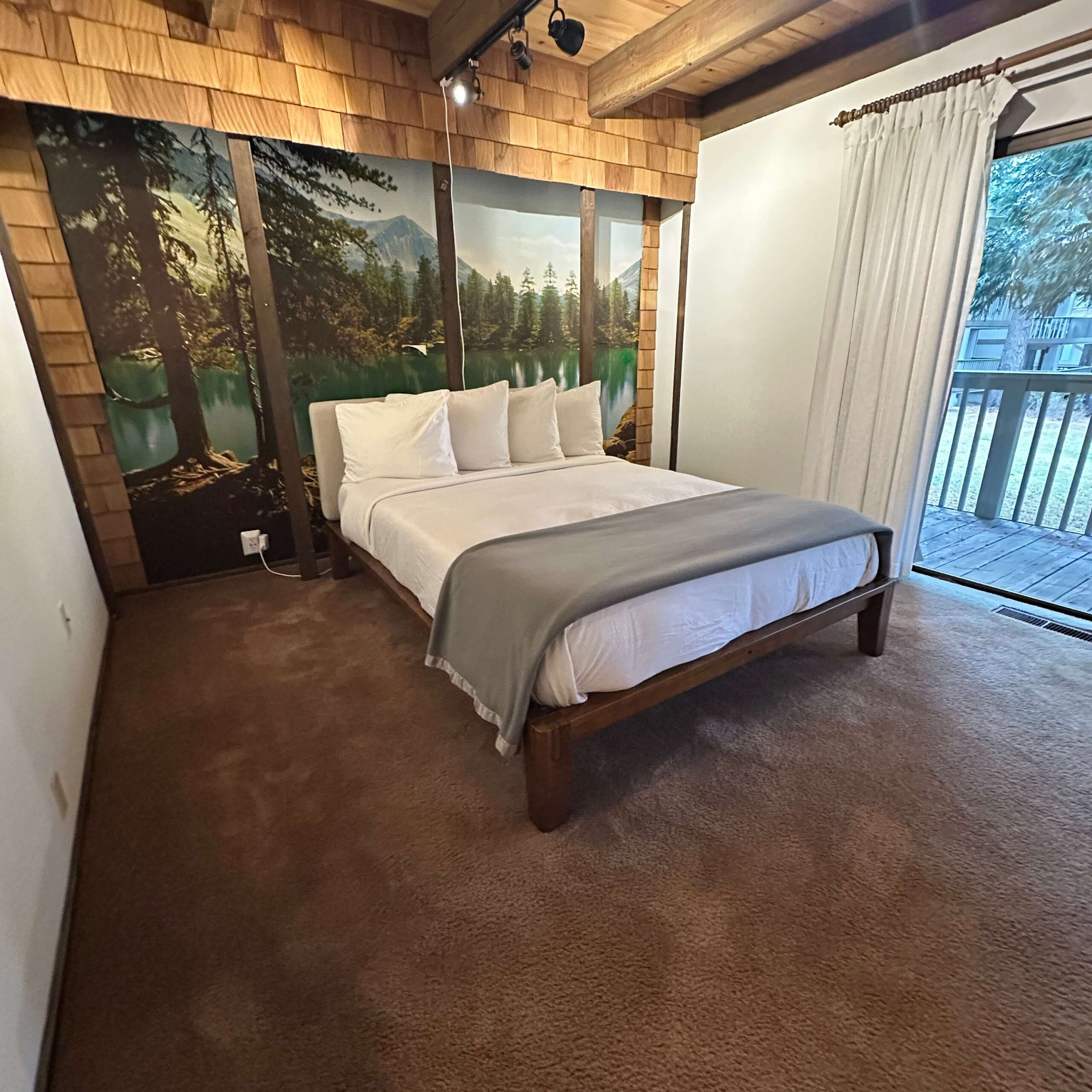 Bedroom in a Kings Beach vacation rental with nature mural, cozy bed, and sliding glass door leading to a balcony.