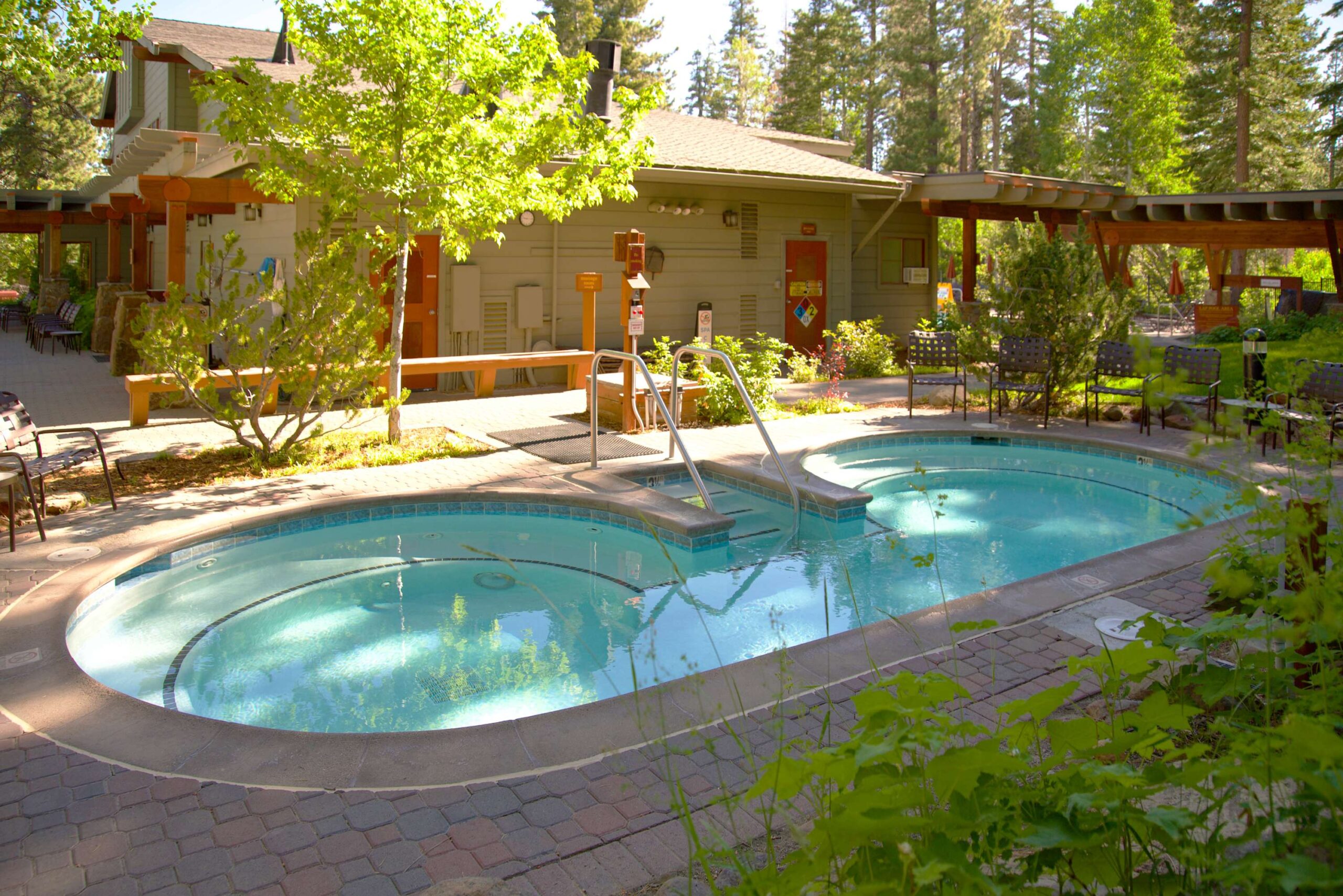 Outdoor pool area at a Truckee vacation rental, surrounded by trees and patio seating, with a rustic building nearby.