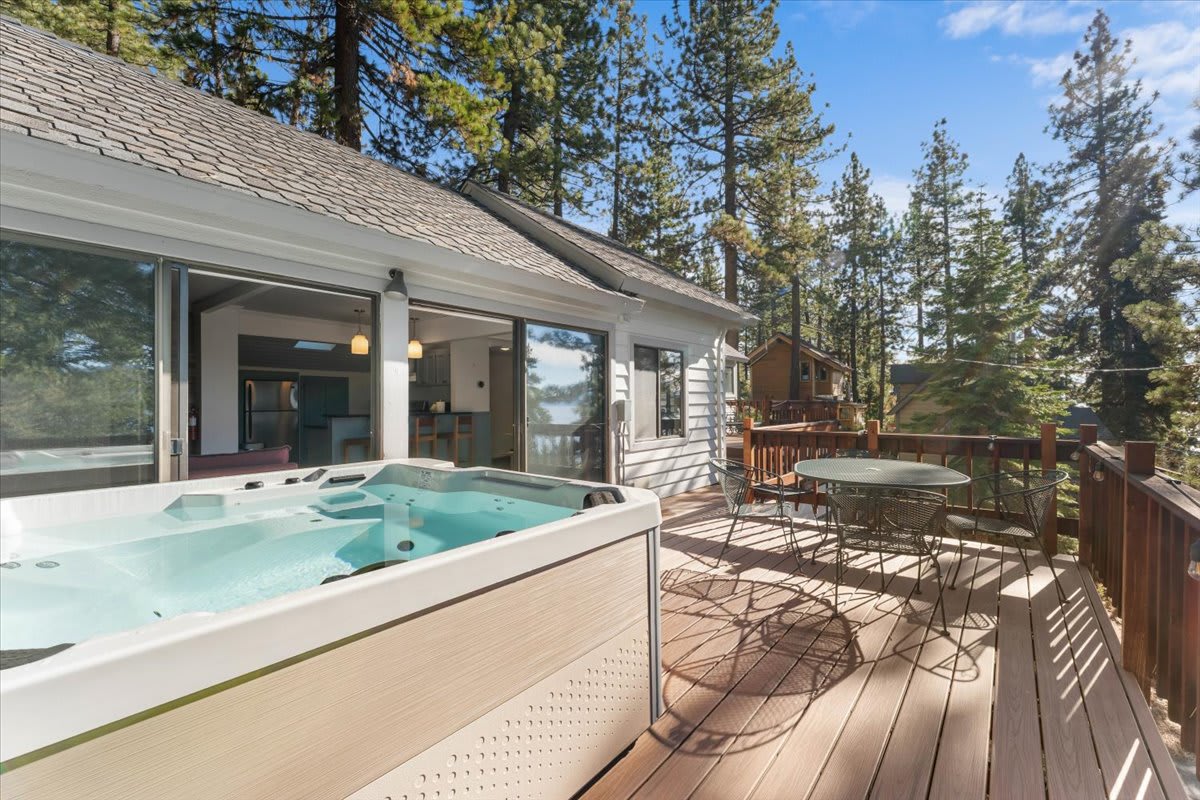 Kings Beach vacation rental deck with hot tub and seating, surrounded by pine trees under a clear blue sky.