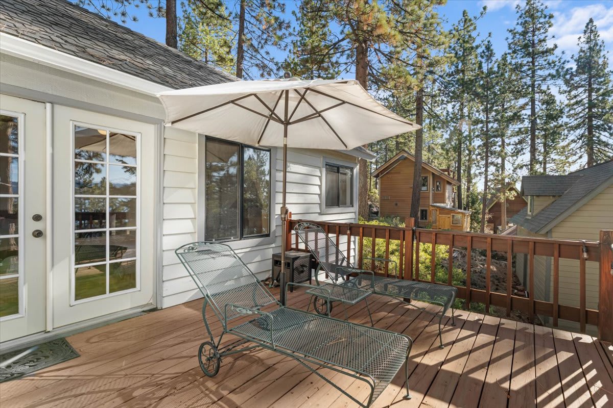 Kings Beach vacation rental patio with lounge chairs, umbrella, and view of the forest and neighboring houses.