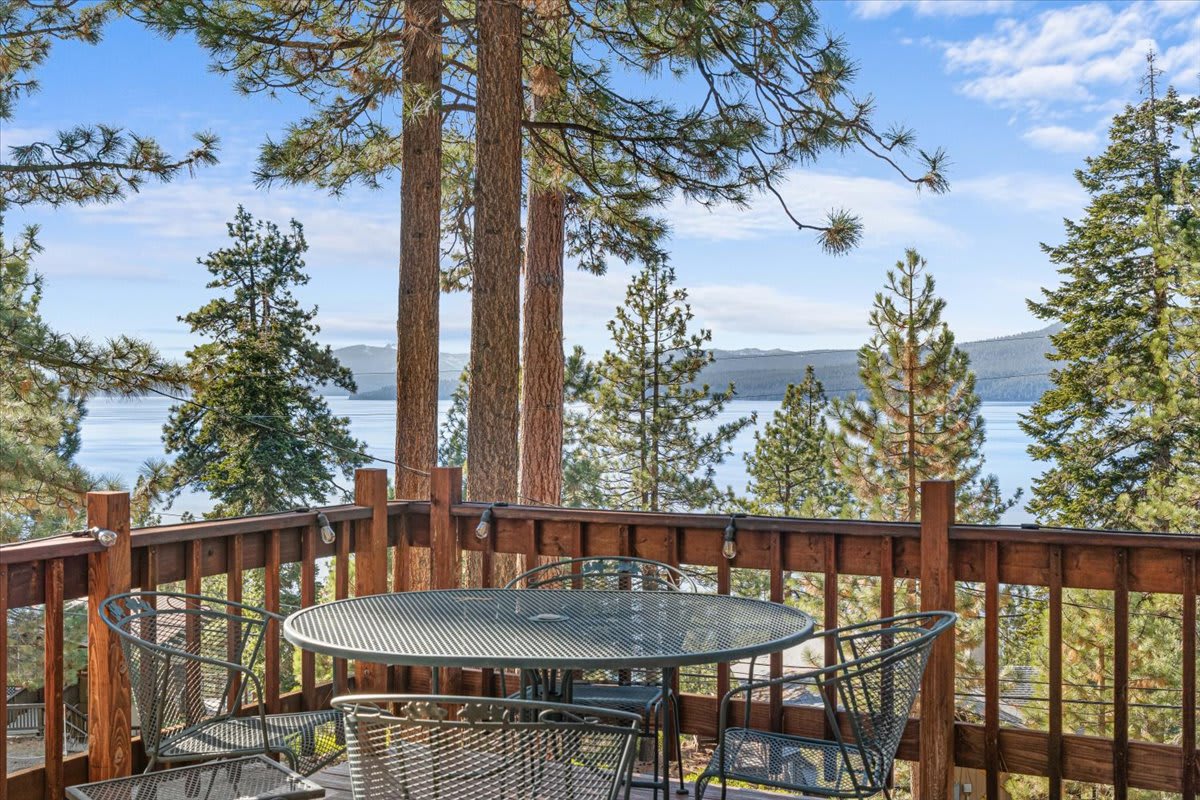 Kings Beach vacation rental deck with lake view, surrounded by tall pine trees and metal chairs around a table.