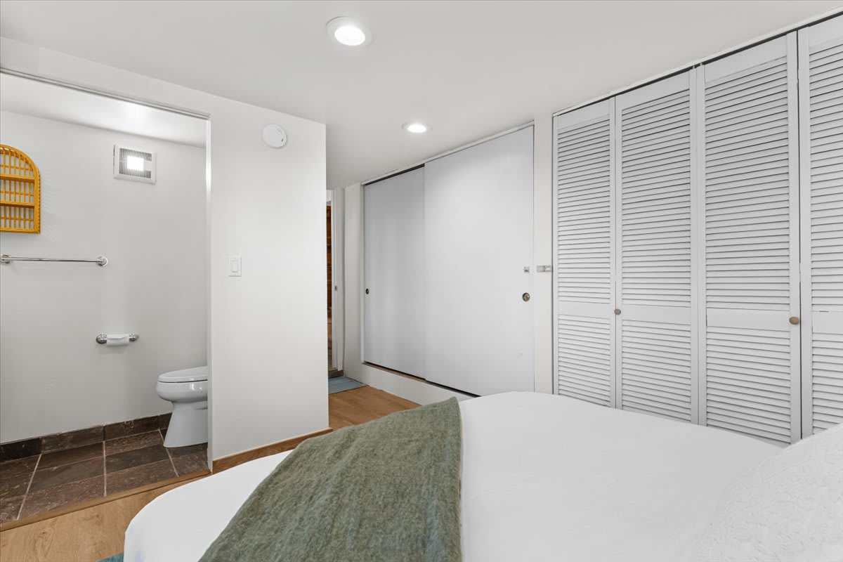Kings Beach vacation rental bedroom with white closet doors, bed, and view into an adjacent bathroom with tiled floor.