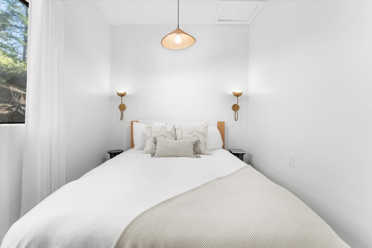 Minimalist bedroom with white bedding and decor in a Kings Beach vacation rental, featuring wall sconces and a window view.