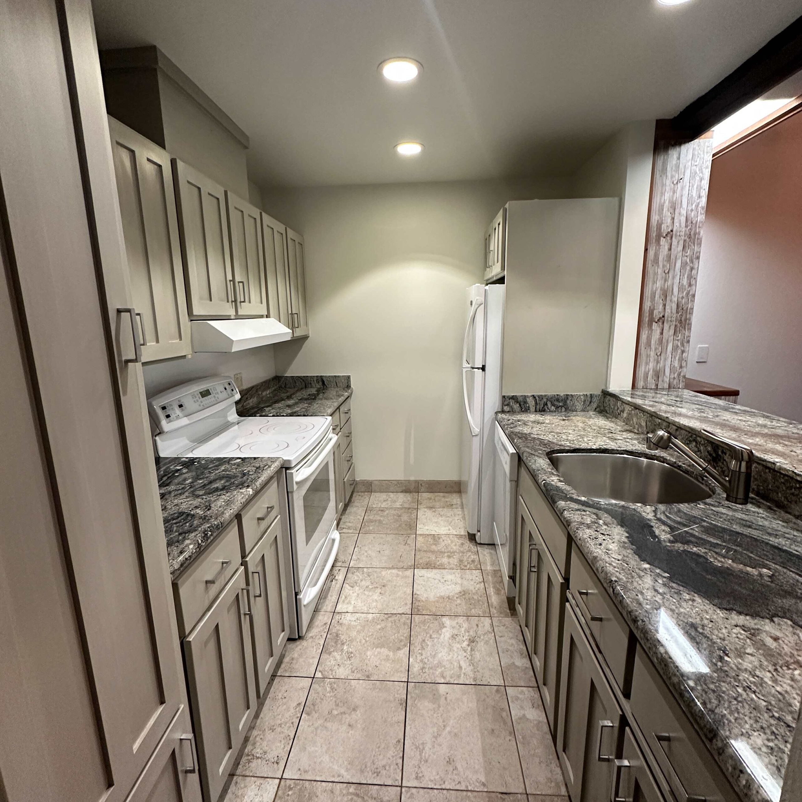 Modern kitchen with granite counters in Kings Beach vacation rental, featuring tiled floor and white appliances.