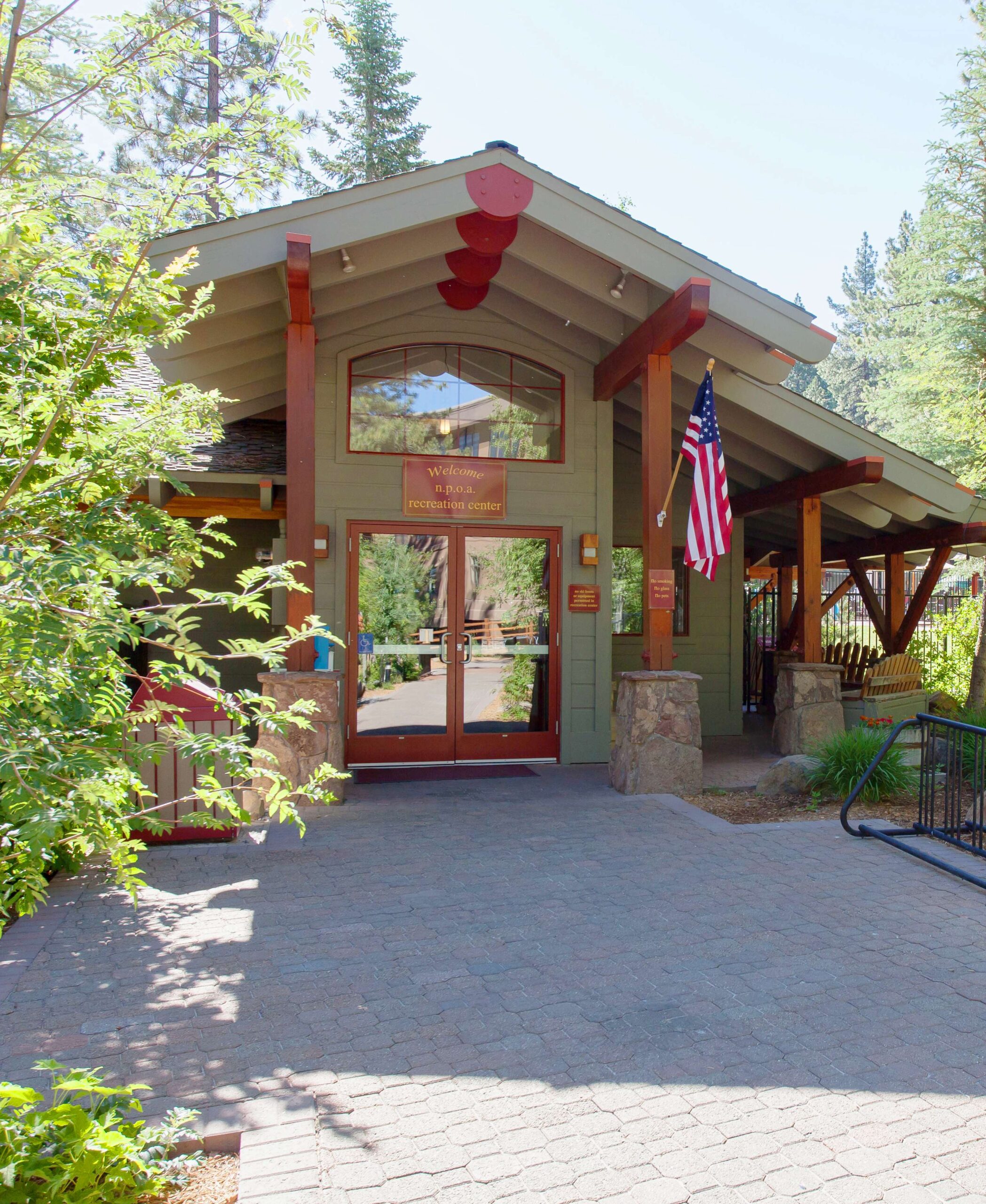 Front of a Truckee vacation rental with American flag, surrounded by trees and a sunny brick pathway.