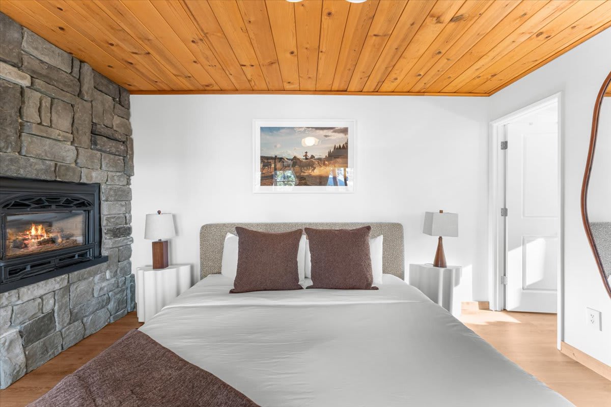Kings Beach vacation rental bedroom with cozy fireplace, wooden ceiling, and stylish decor.