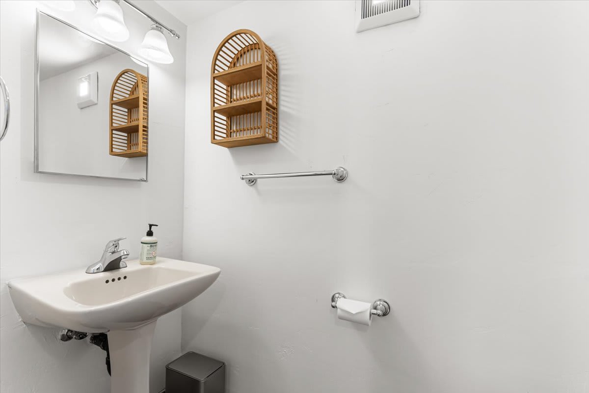 Minimalist bathroom in a Kings Beach vacation rental with a pedestal sink, wooden shelf, and contemporary fixtures.