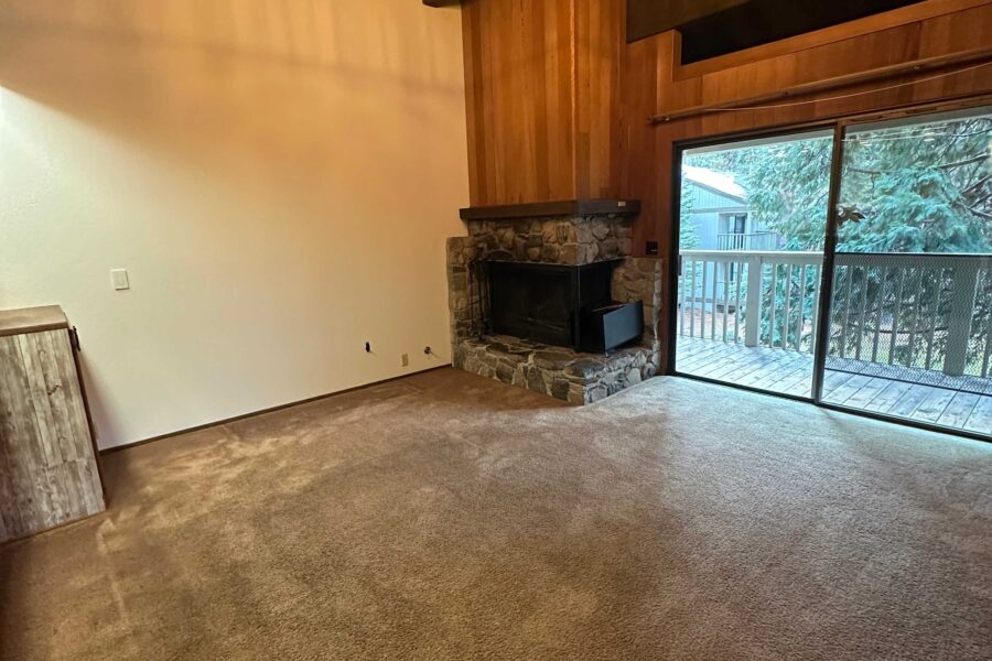 Cozy Kings Beach vacation rental with a stone fireplace and big windows overlooking a wooden balcony and trees.