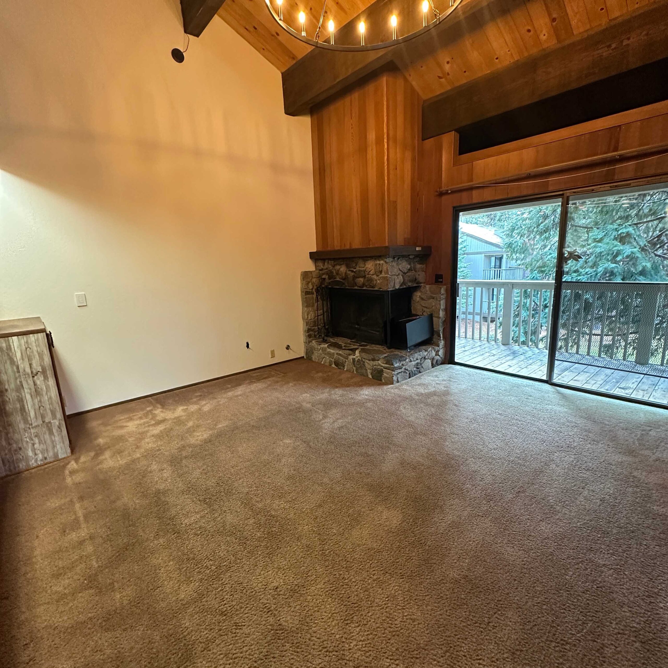 Cozy Kings Beach vacation rental with a stone fireplace and big windows overlooking a wooden balcony and trees.