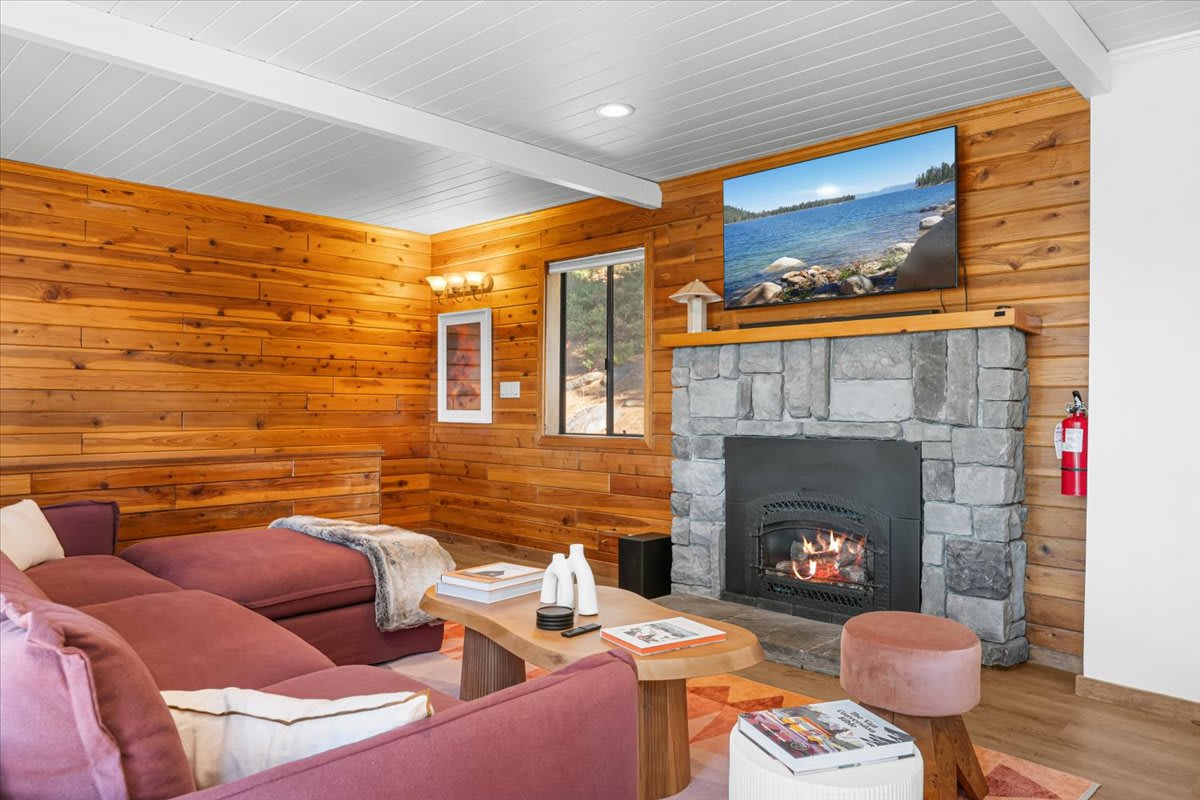 Cozy living room in Kings Beach vacation rental with a stone fireplace, wood paneling, and a large TV above the mantel.