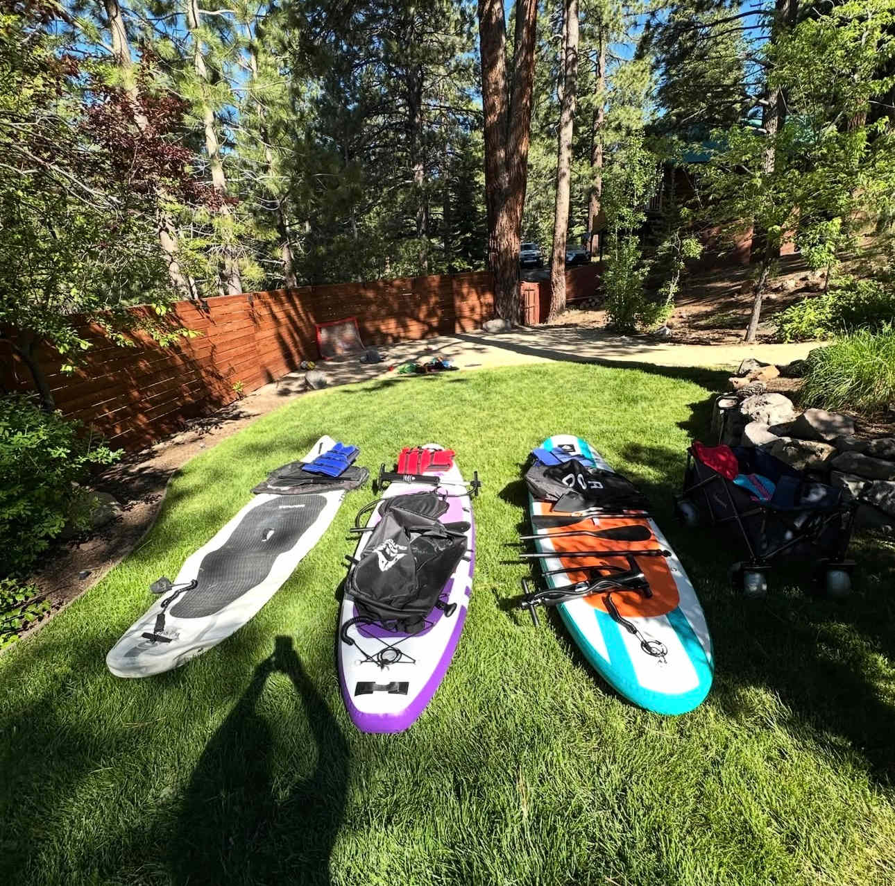 Paddleboards and gear on a lawn at a Truckee vacation rental, surrounded by trees and wooden fencing.