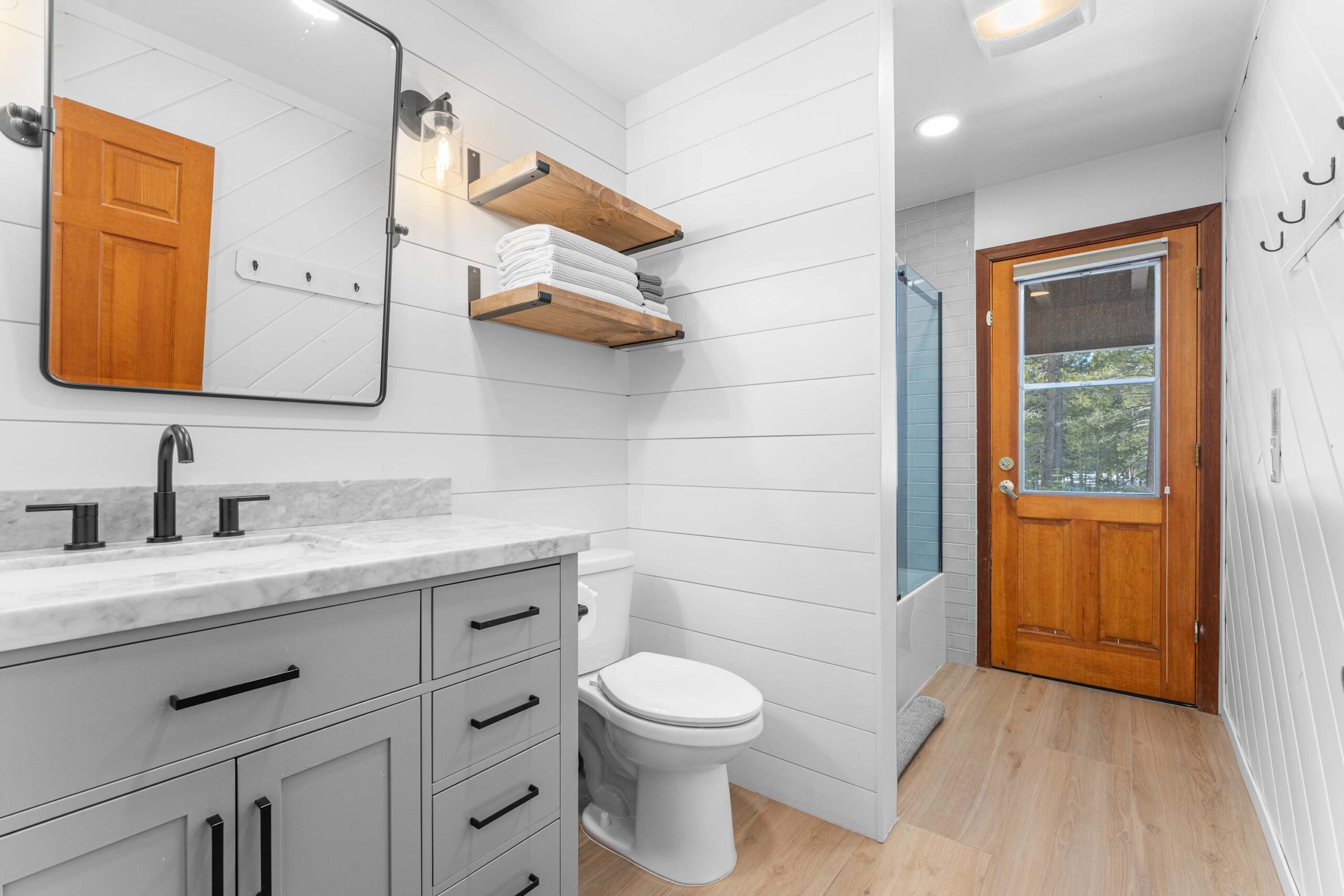 Modern bathroom in a Truckee vacation rental featuring a marble-topped vanity, wooden shelves, and a door to outside.