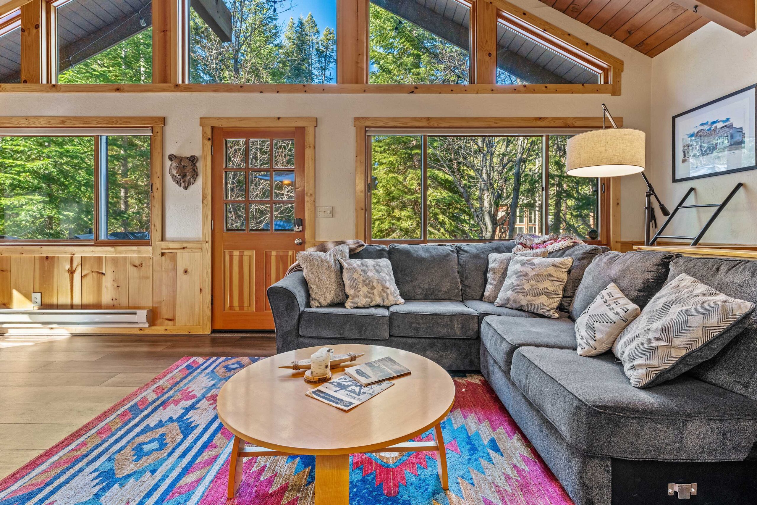 Cozy Truckee vacation rental living room with a sectional sofa, colorful rug, and large windows with forest views.
