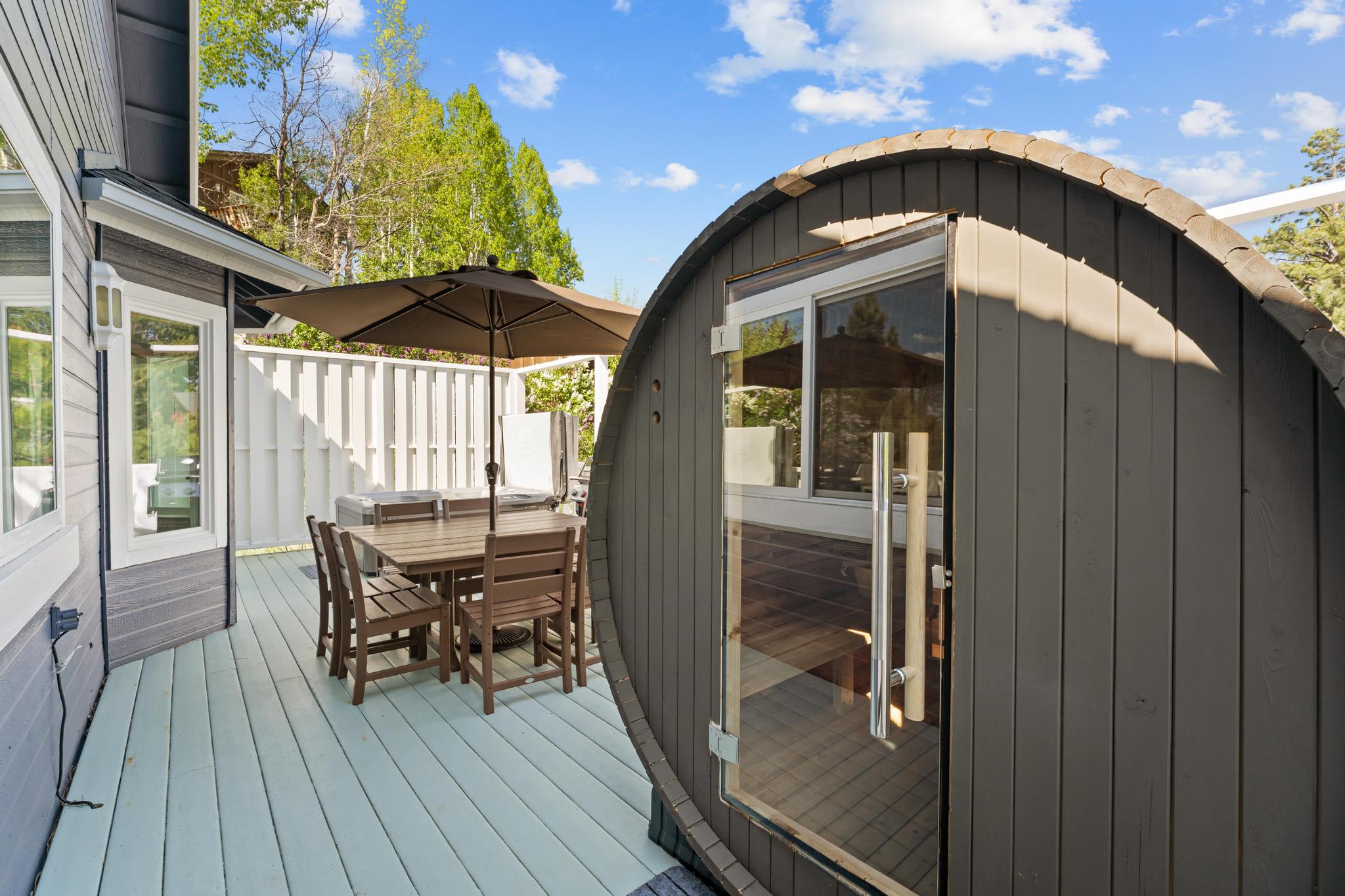 Outdoor deck of a Truckee vacation rental featuring a wooden sauna and dining area under a large umbrella.