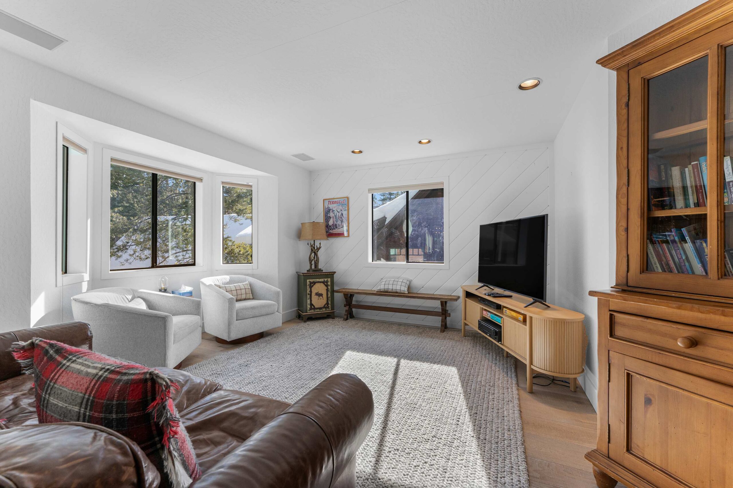 Cozy living room in Truckee vacation rental with leather couch, armchairs, TV, and large windows overlooking trees.