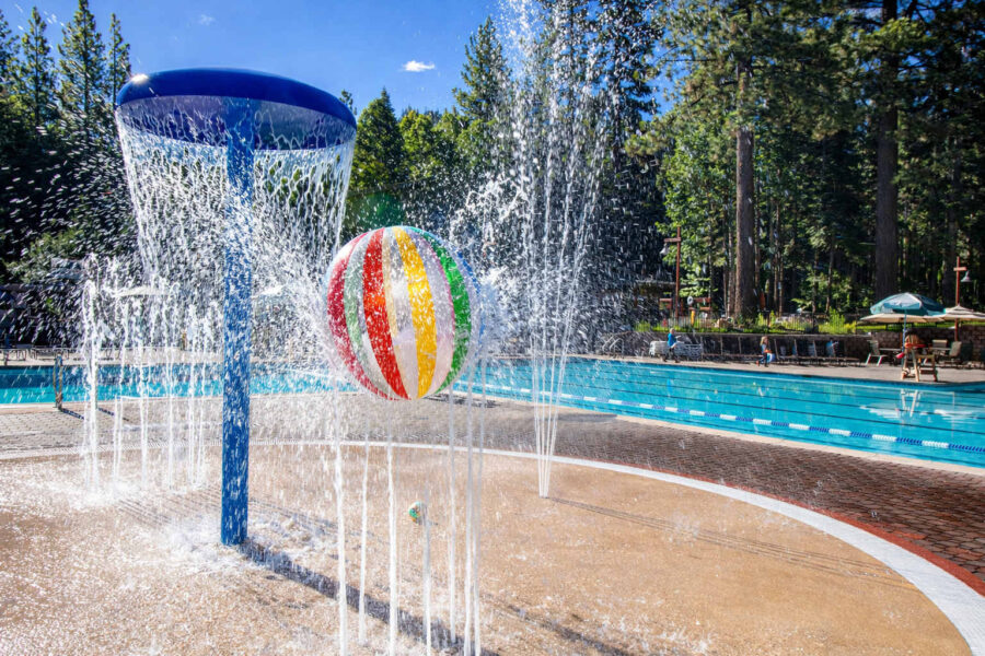 Pool area at a Truckee vacation rental with a splash fountain and colorful beach ball amidst tall trees.