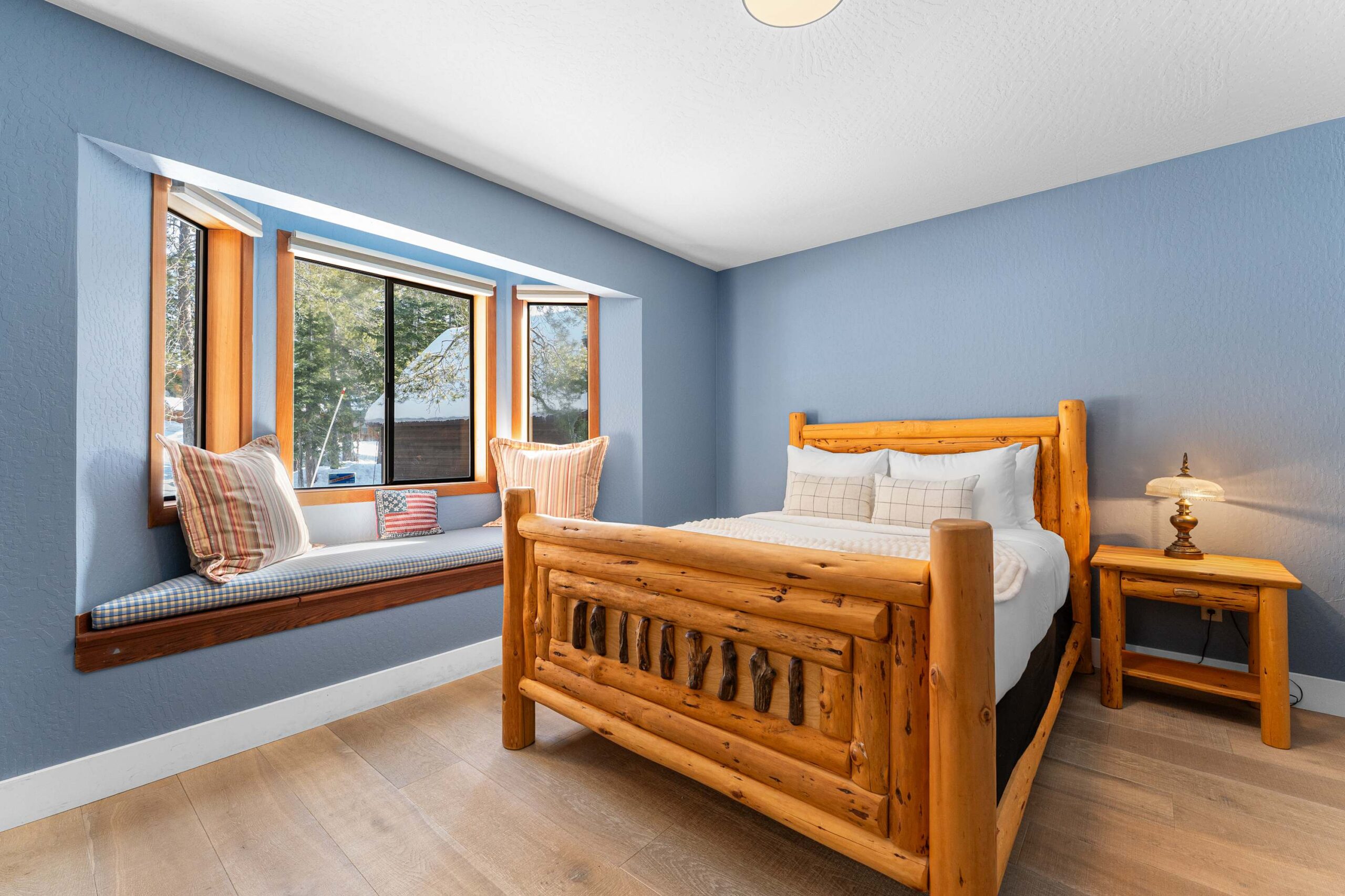 Cozy bedroom in a Truckee vacation rental with rustic wood bed, side table, blue walls, and a window seat.