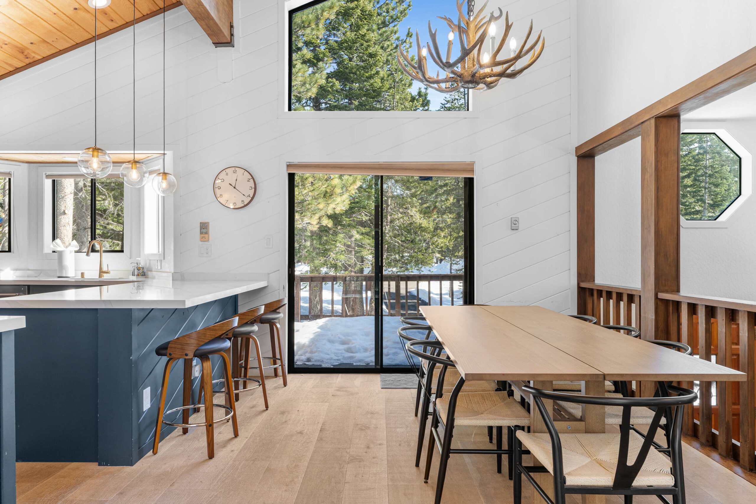 Modern kitchen and dining area in a cozy Truckee vacation rental, with large windows overlooking snowy trees.