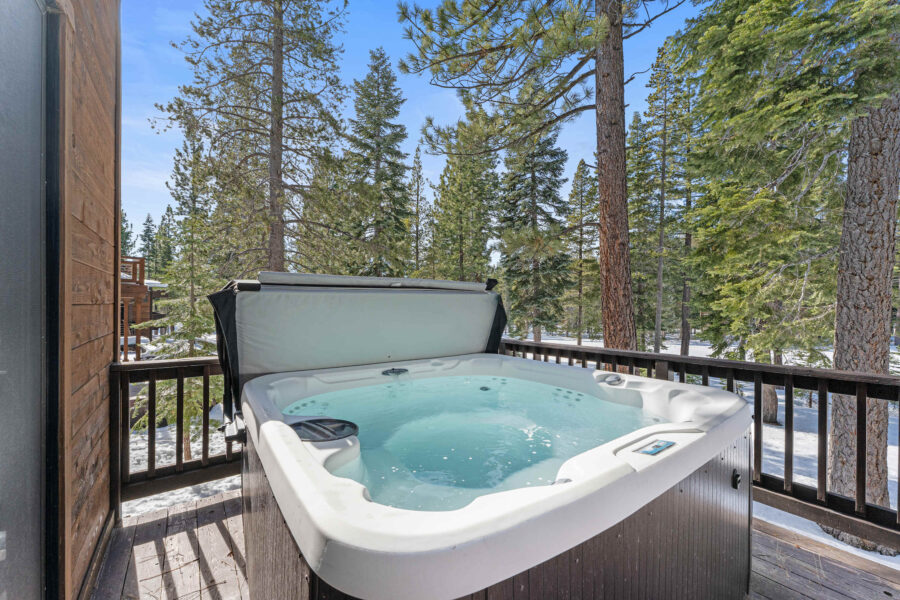 Hot tub on wooden deck with forest view at a Truckee vacation rental, surrounded by tall pine trees and clear blue sky.