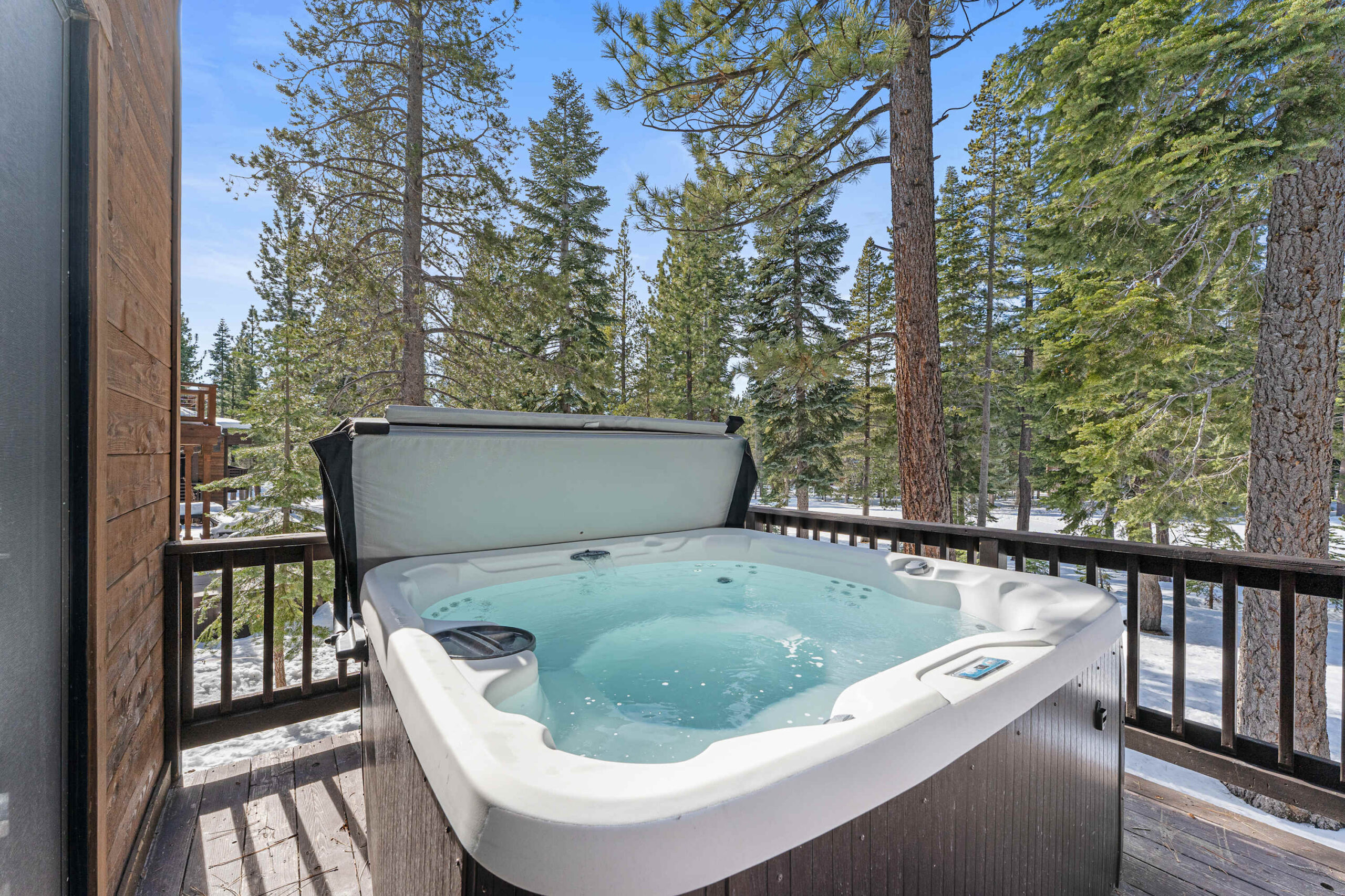 Hot tub on wooden deck with forest view at a Truckee vacation rental, surrounded by tall pine trees and clear blue sky.