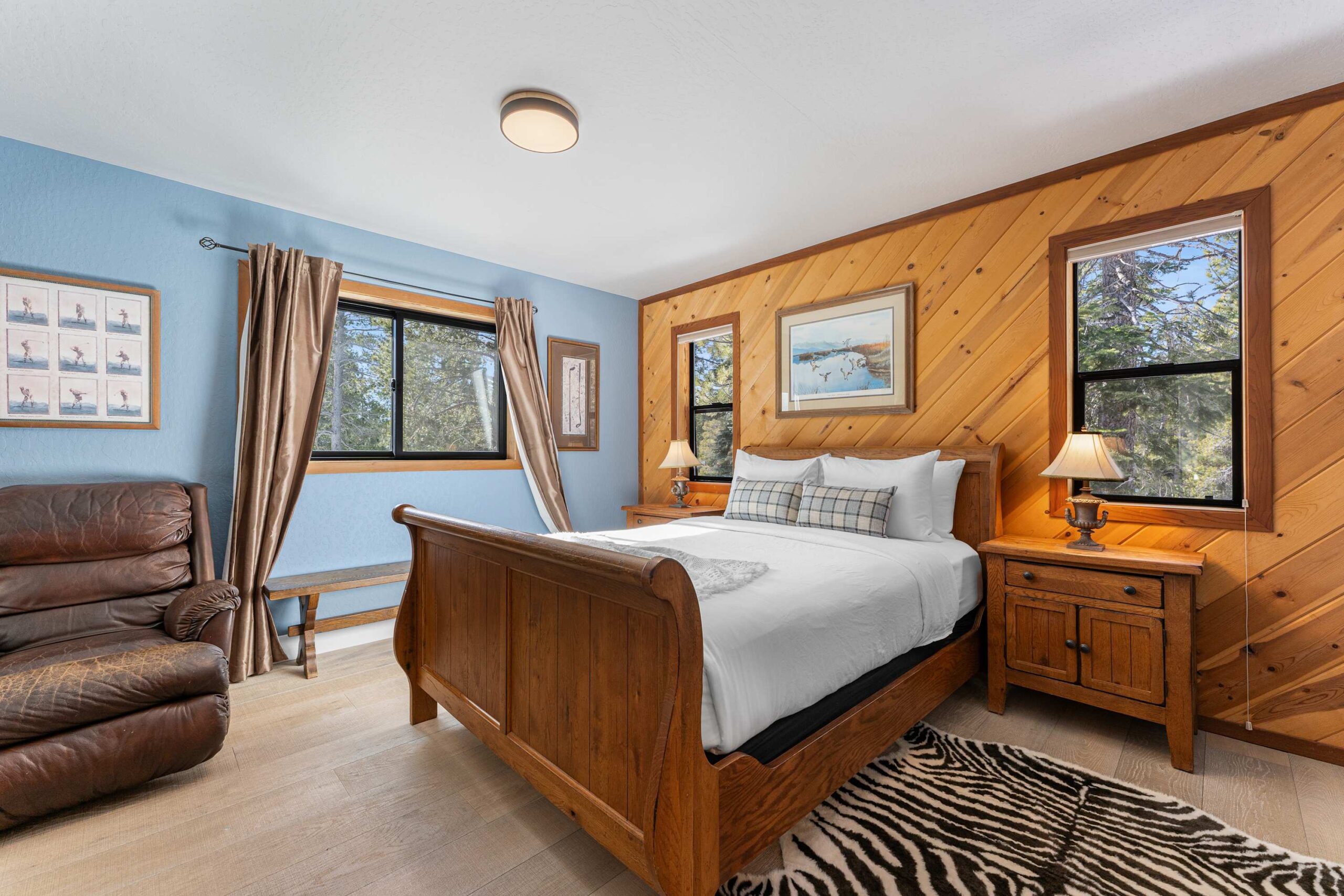 Cozy Truckee vacation rental bedroom with wooden accents, comfy bed, leather chair, and forest views through large windows.