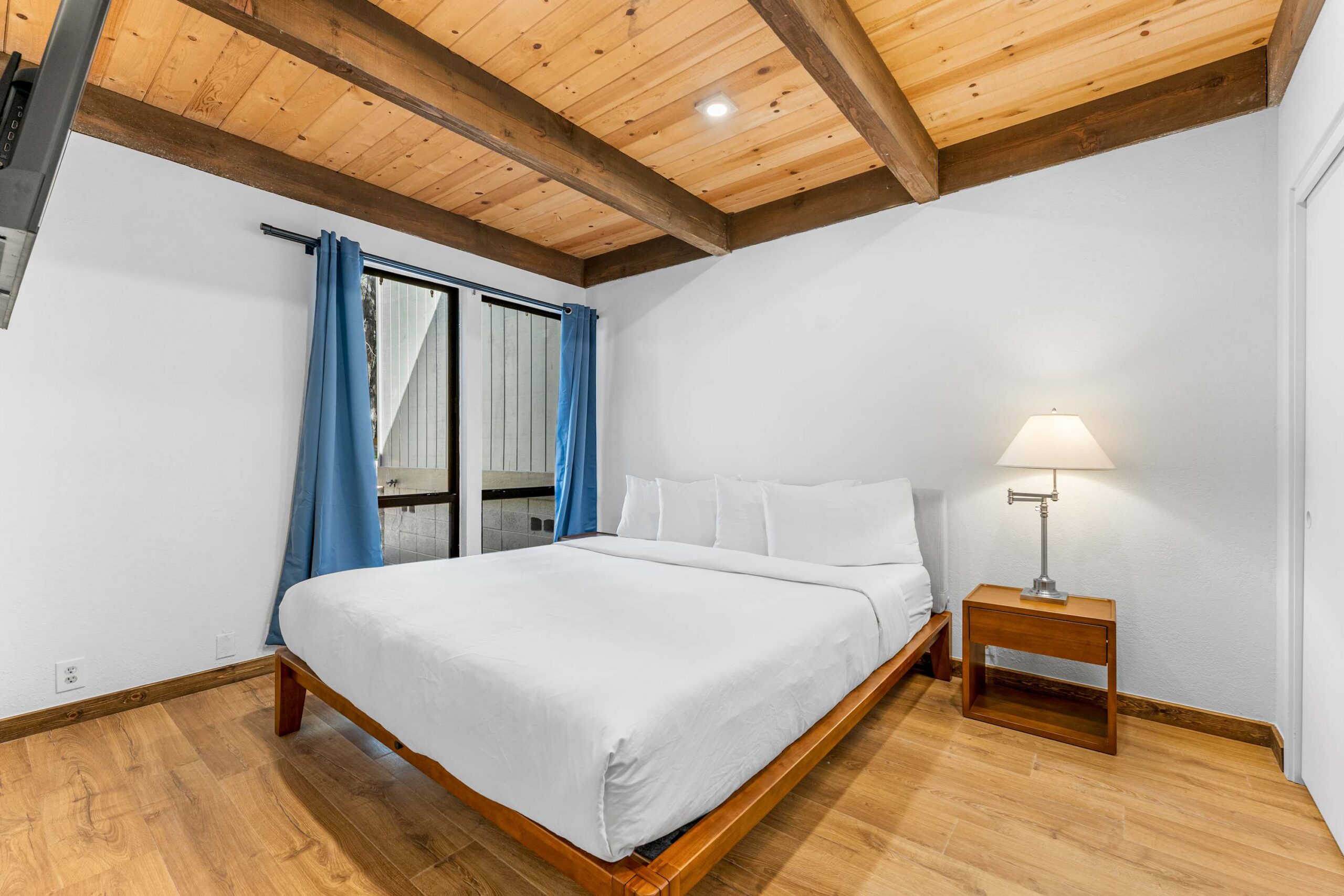 Modern bedroom in a Kings Beach vacation rental, featuring a wooden bed, blue curtains, and cozy ambiance.