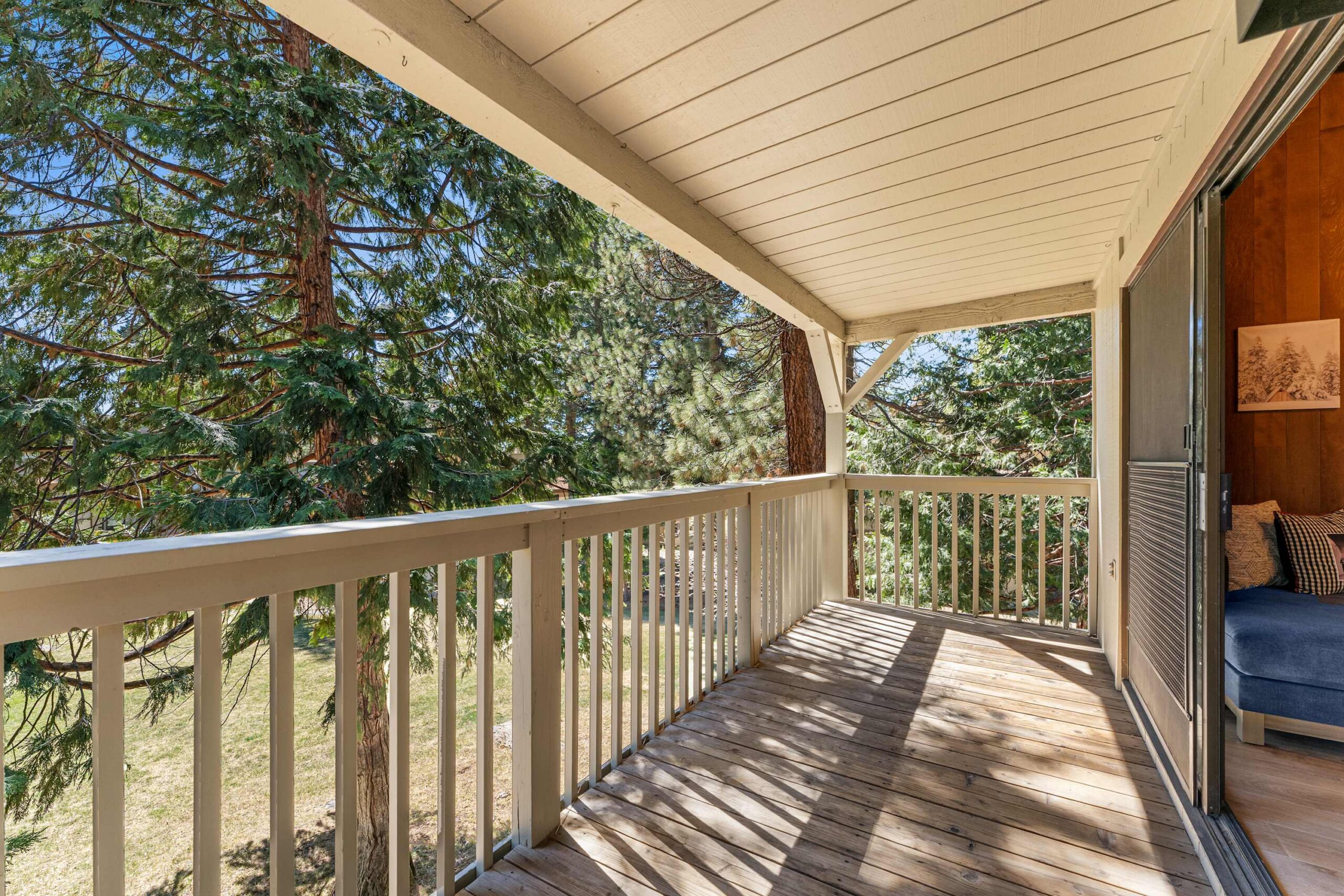 Covered balcony of a vacation rental in Kings Beach, overlooking trees and natural scenery. Cozy seating visible inside.