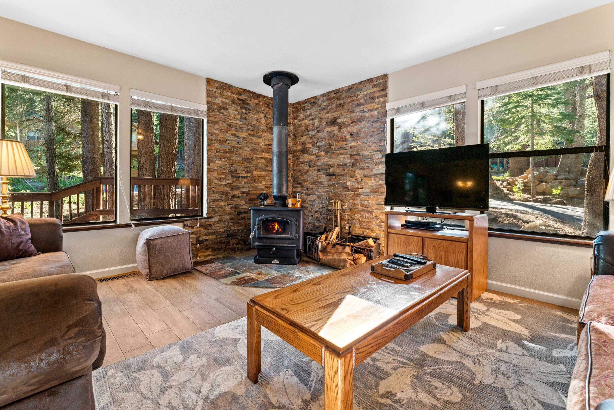Cozy Truckee vacation rental living room with wood stove, TV, and forest view through large windows.
