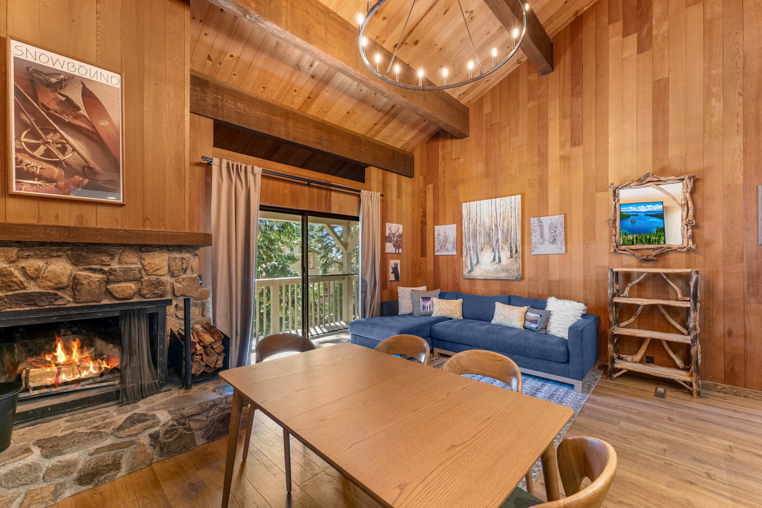 Wooden interior of a Kings Beach vacation rental with a stone fireplace, blue sofa, and sliding door to a balcony.