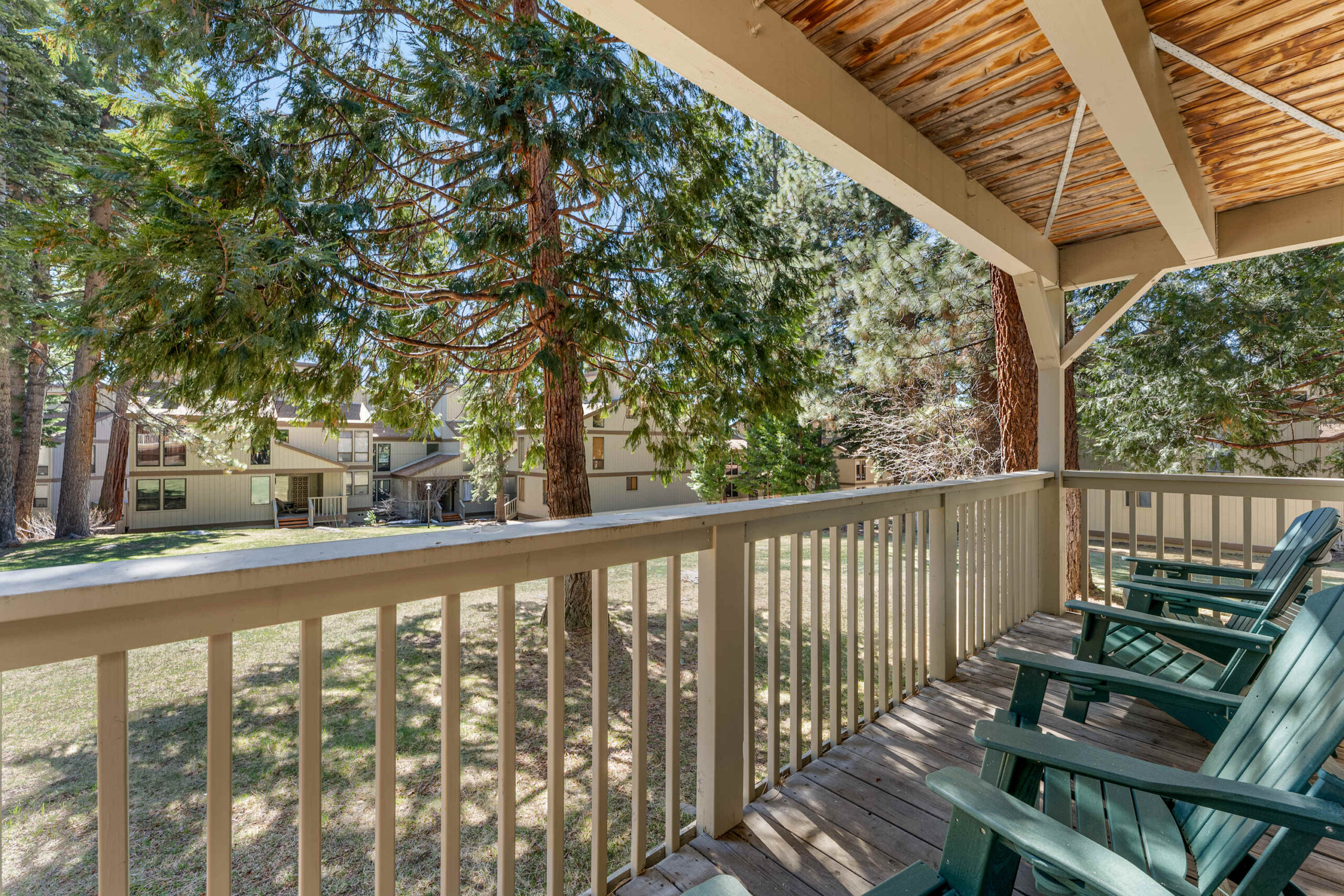 Deck view from a Kings Beach vacation rental, featuring green chairs and overlooking trees and nearby houses.