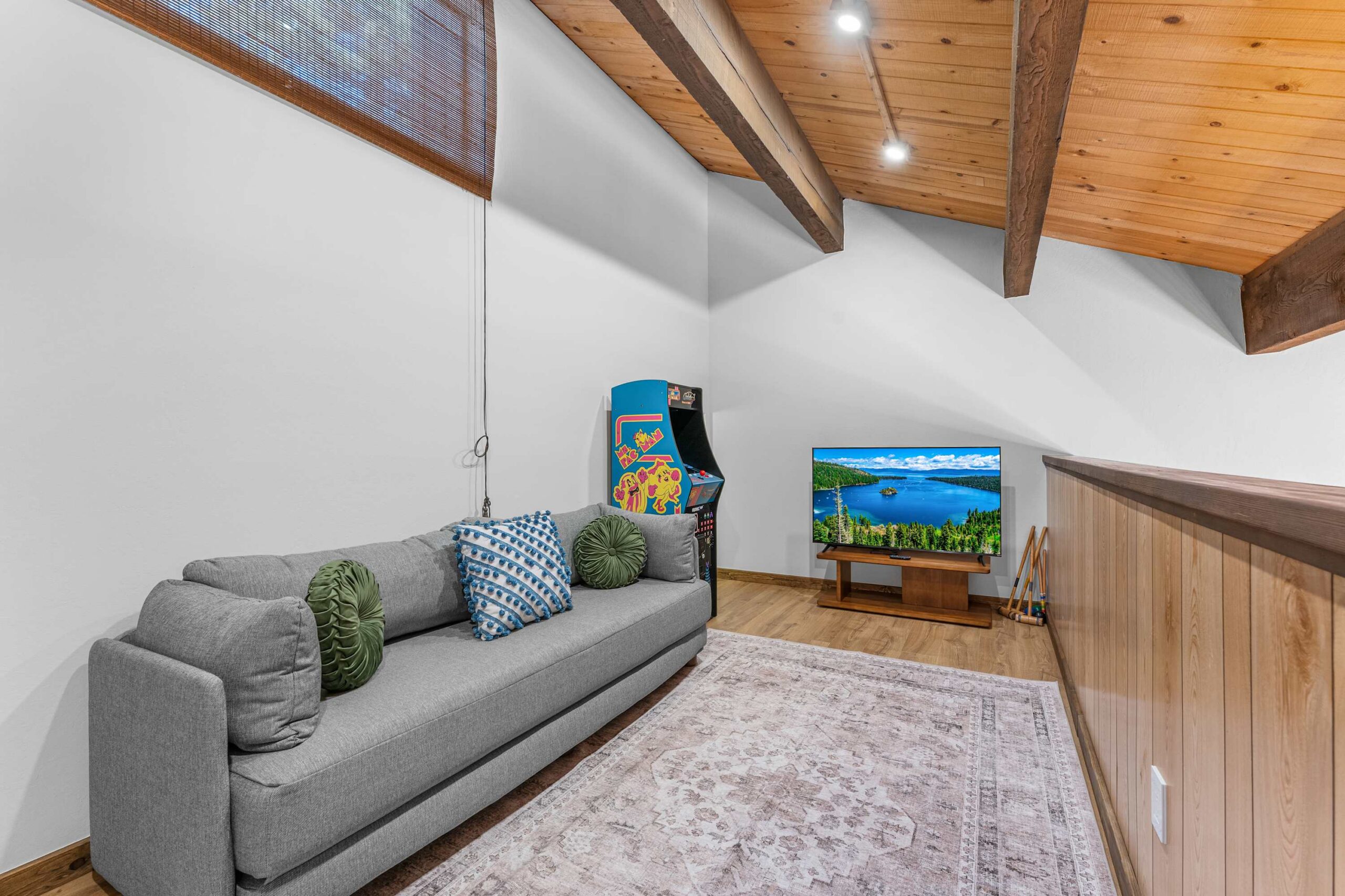 Kings Beach vacation rental with cozy loft, gray sofa, arcade game, and TV displaying a scenic lake view.