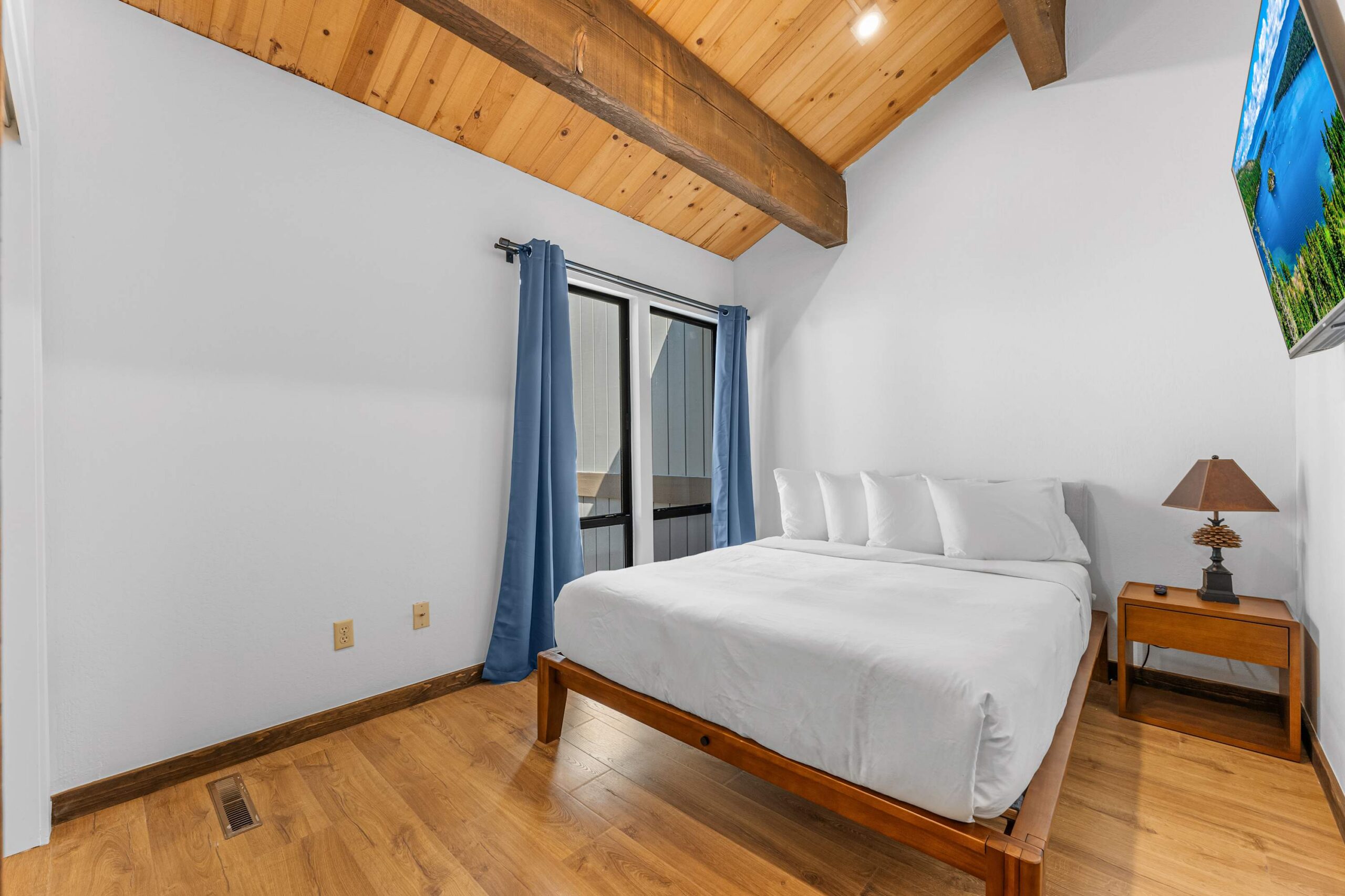 Cozy bedroom in a Kings Beach vacation rental with wood ceilings, a double bed, blue curtains, and a wooden nightstand.