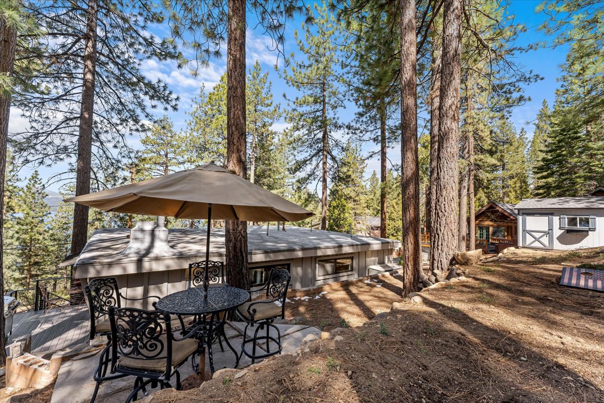 Patio with umbrella and chairs outside a vacation rental in a forested area of Kings Beach, under clear blue skies.