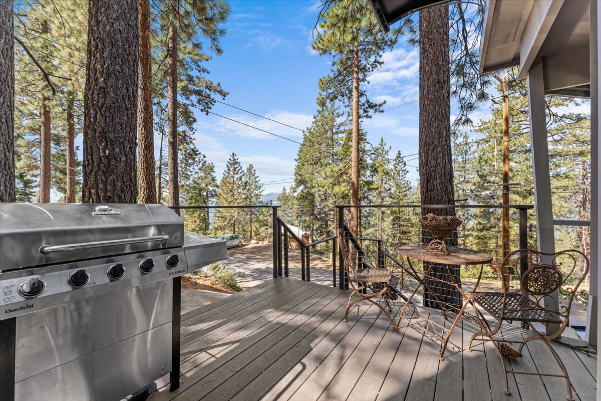 Deck of a Kings Beach vacation rental with grill, table, and chairs overlooking pine trees.