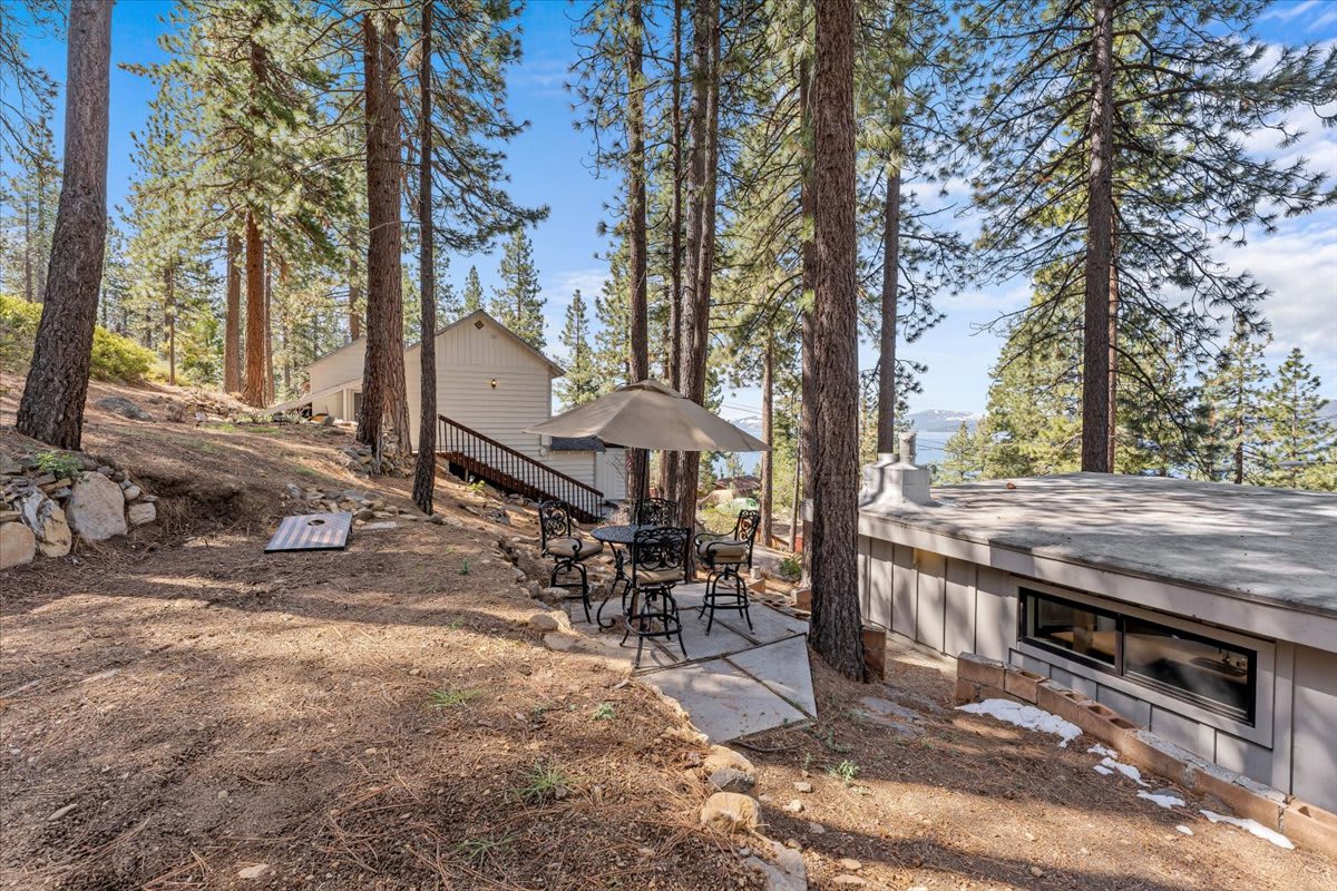 Outdoor seating and umbrella at a Kings Beach vacation rental surrounded by tall pines with a view of the lake.