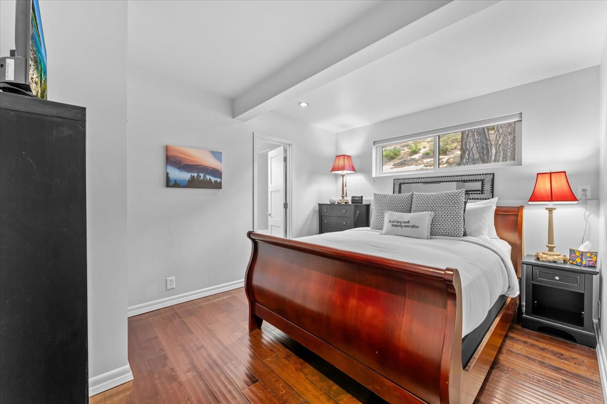 Elegantly decorated bedroom of a Kings Beach vacation rental with a wooden bed, lamps, and scenic artwork.