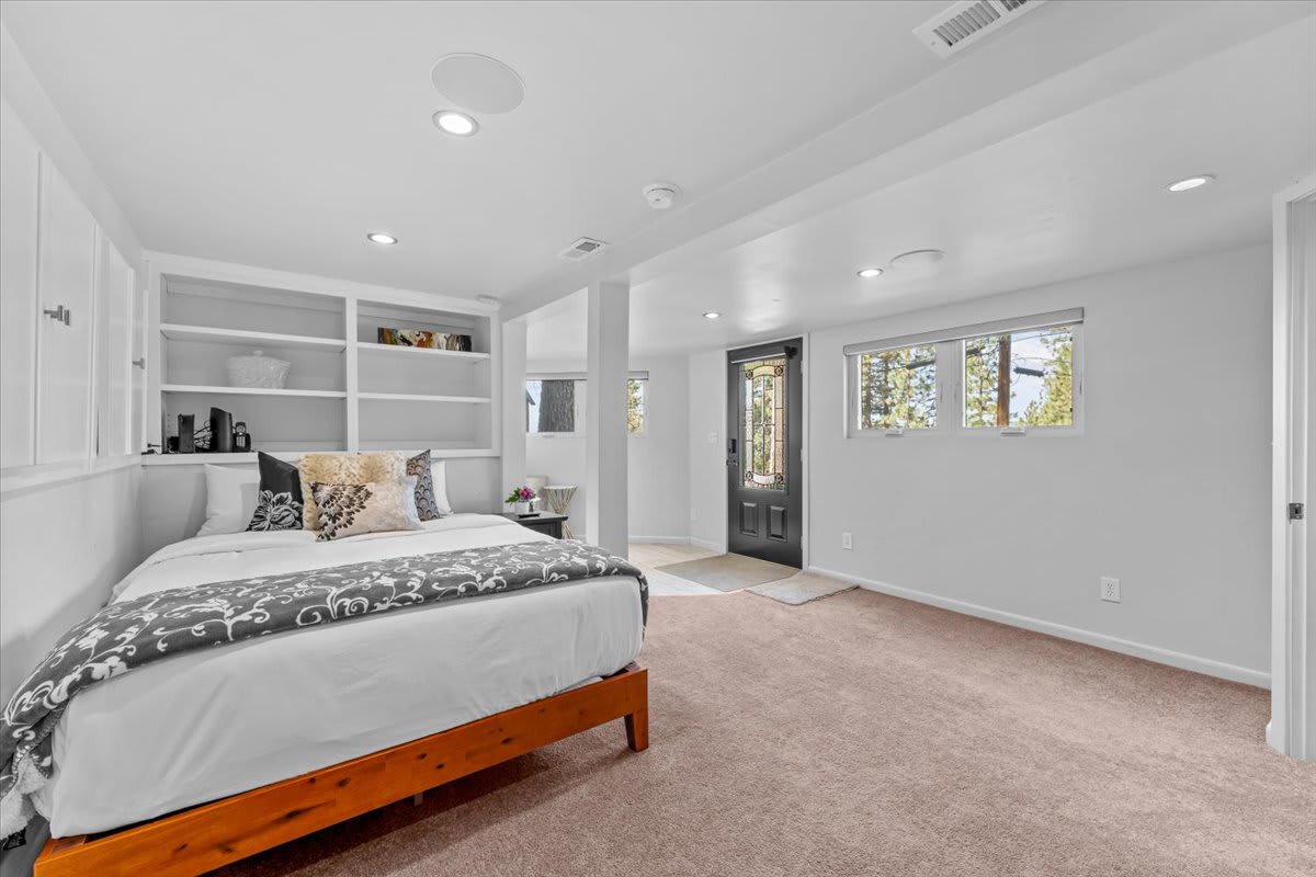 Modern vacation rental bedroom in Kings Beach with cozy bed, built-in shelves, and windows overlooking the natural scenery.