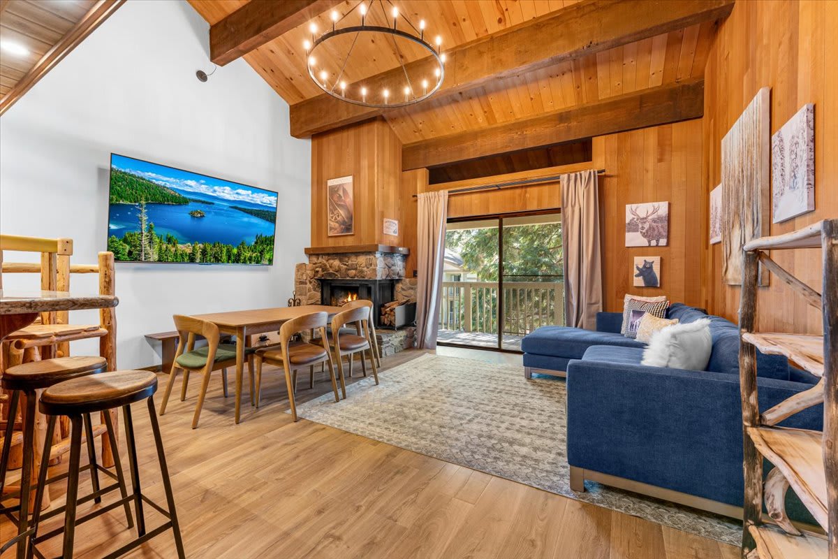 Cozy living area in a Kings Beach vacation rental with wood paneling, dining set, fireplace, and large window view.