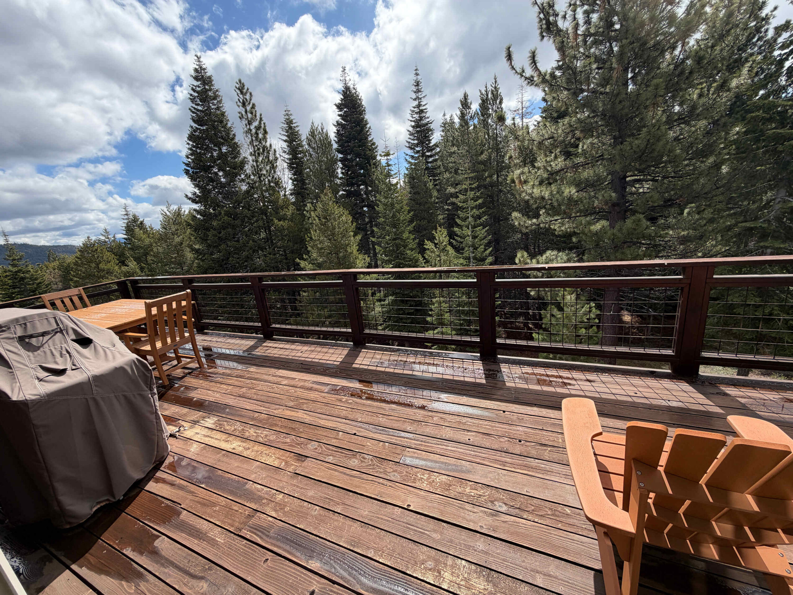 Truckee vacation rental deck with forest view, featuring wooden chairs, table, and a grill under cloudy skies.