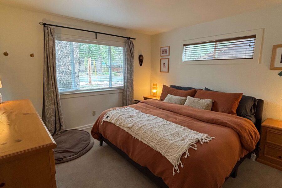 Cozy bedroom in a Truckee vacation rental, featuring a large bed with orange bedding and a view of the wooded outdoors.