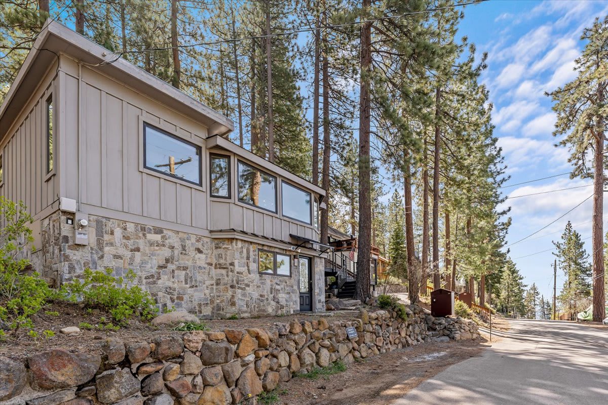 Stone-accented vacation rental surrounded by tall trees in Kings Beach, nestled along a quiet road under a blue sky.
