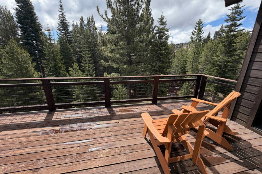 Sunny deck at a Truckee vacation rental with two wooden chairs overlooking lush pine trees.