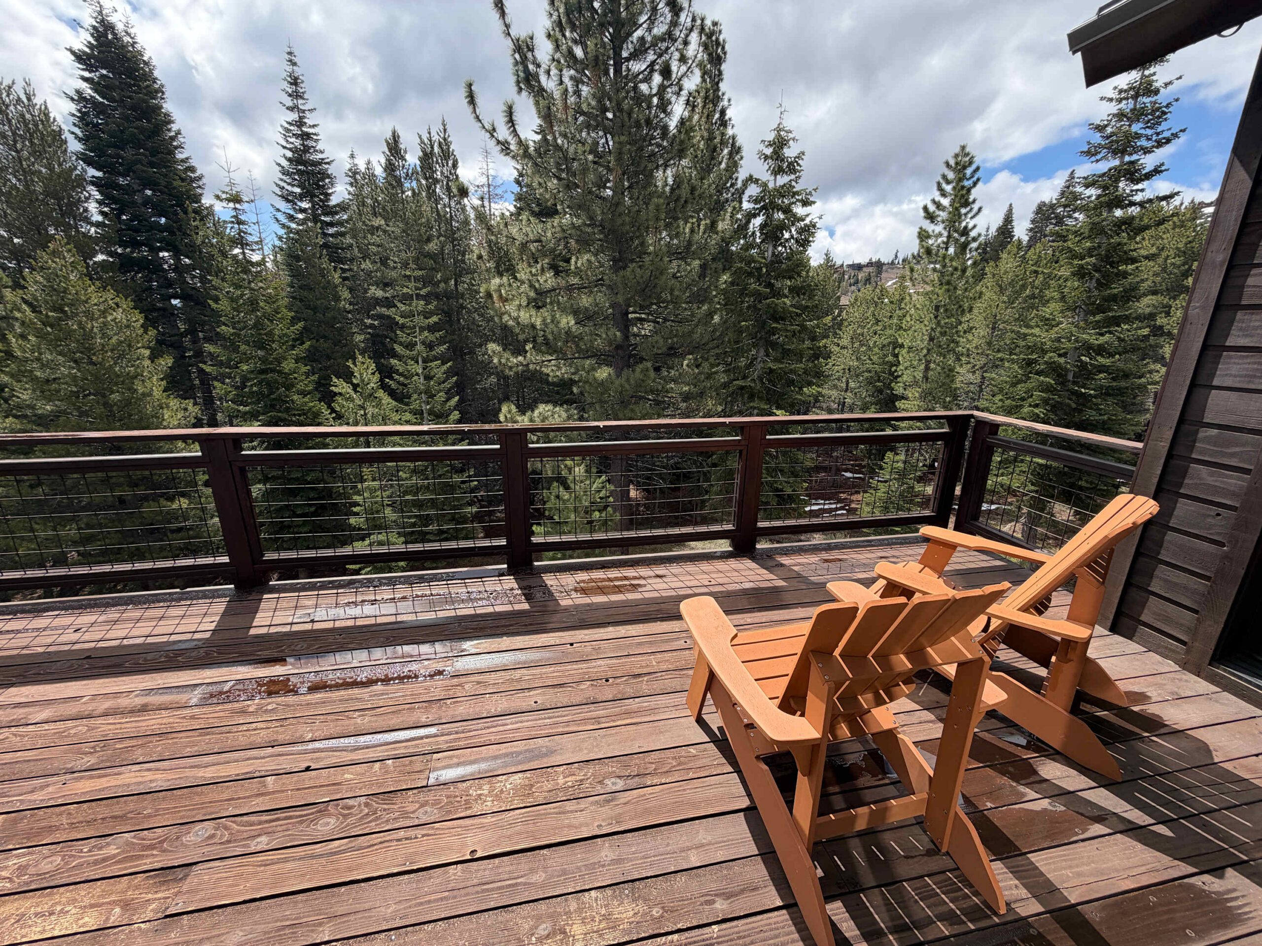 Sunny deck at a Truckee vacation rental with two wooden chairs overlooking lush pine trees.