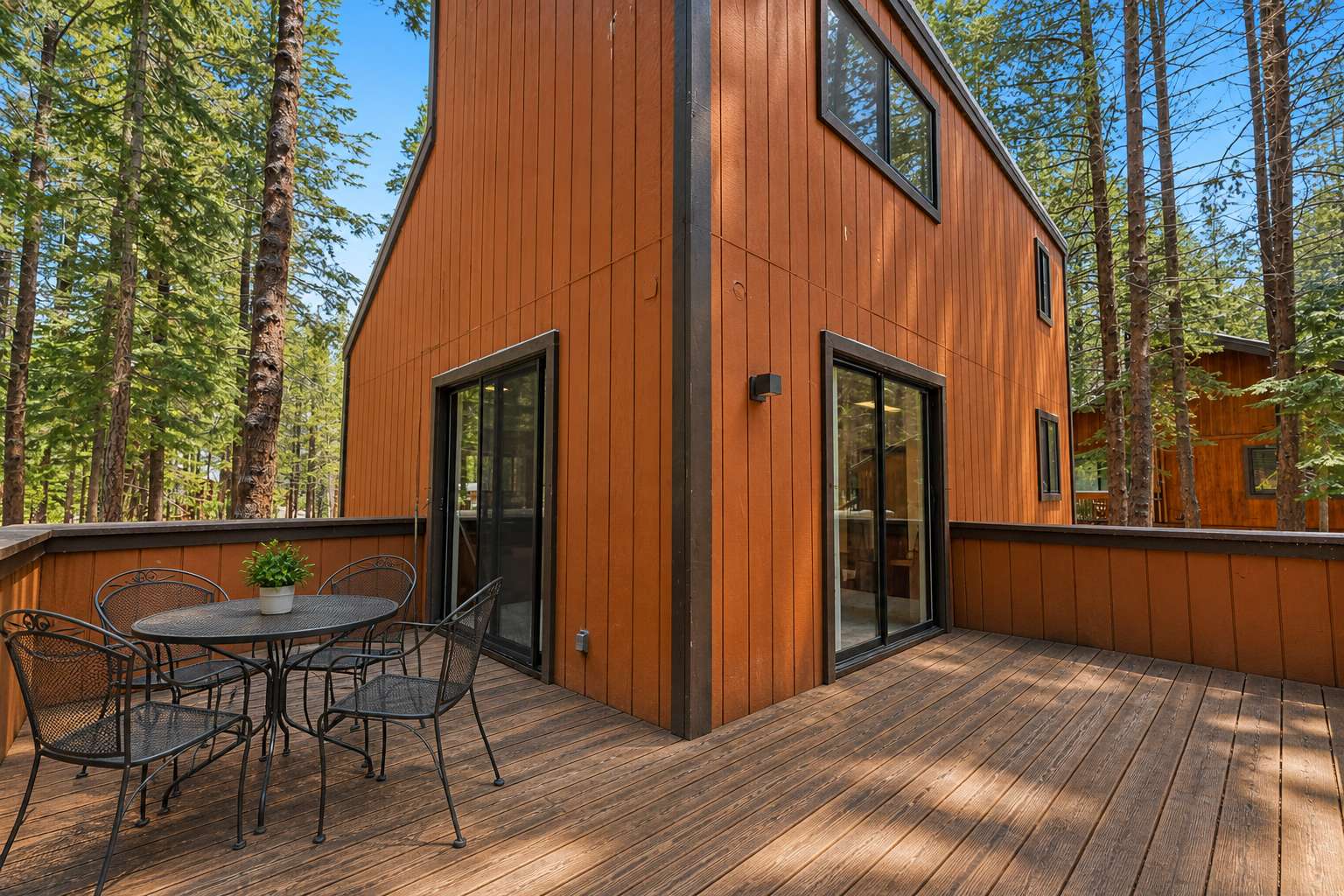 Truckee vacation rental with wooden deck, outdoor table, chairs, surrounded by tall pine trees and clear blue sky.